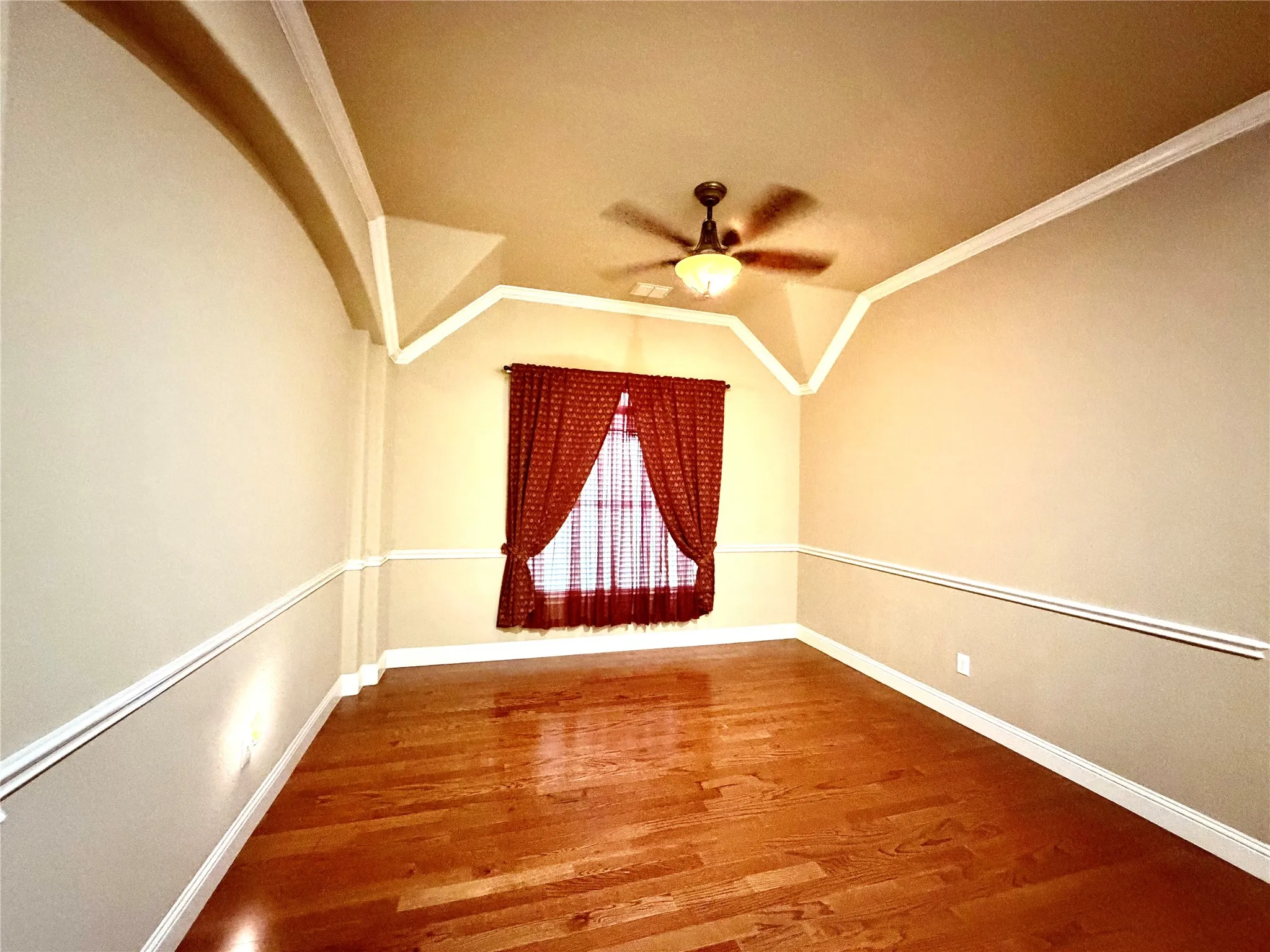 Wood-finish flooring, decorative wall molding, a ceiling fan with integrated lighting, and unique ceiling accents
