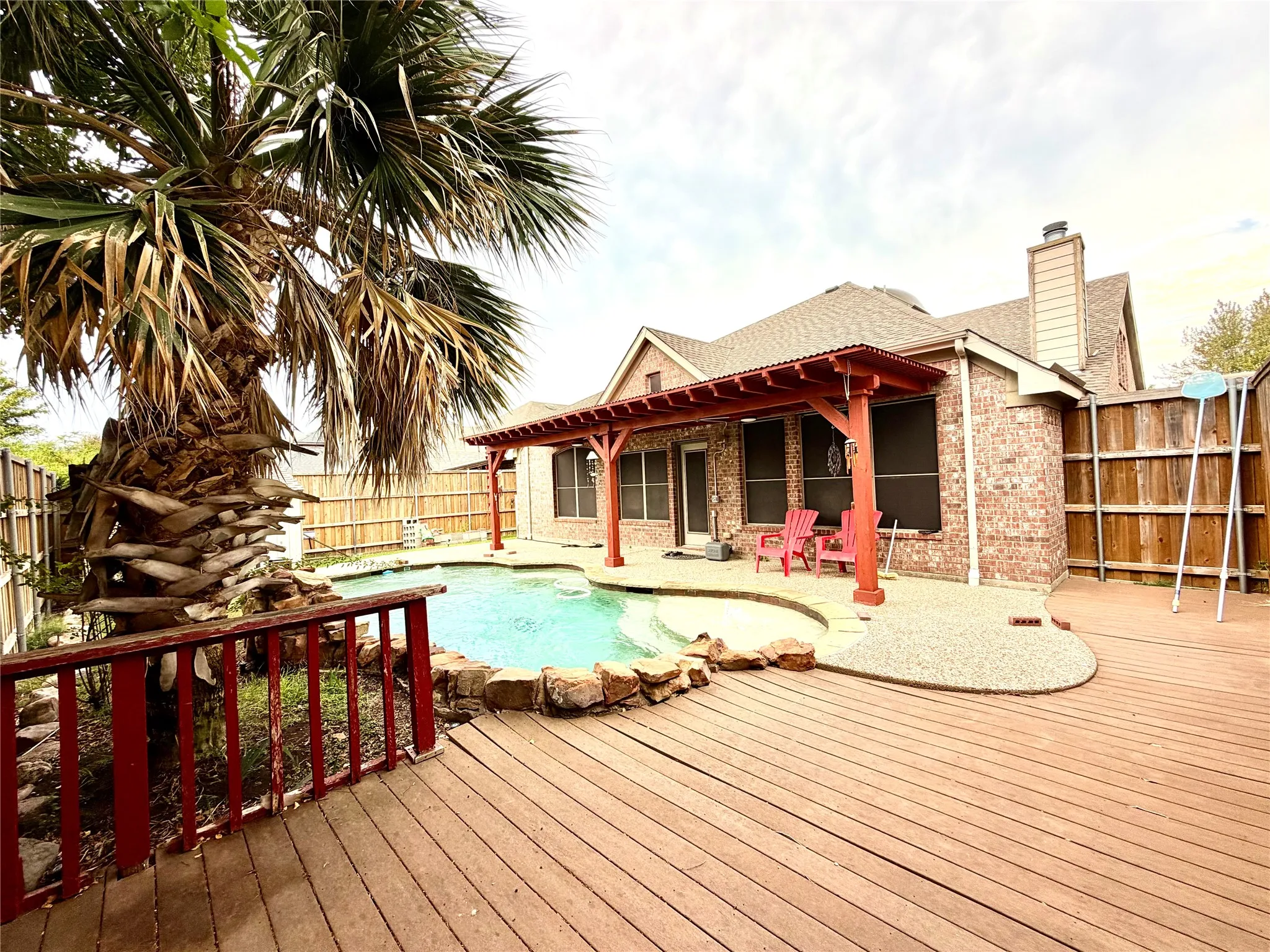 Expansive backyard featuring a large swimming pool, wood deck, and a red wood pergola
