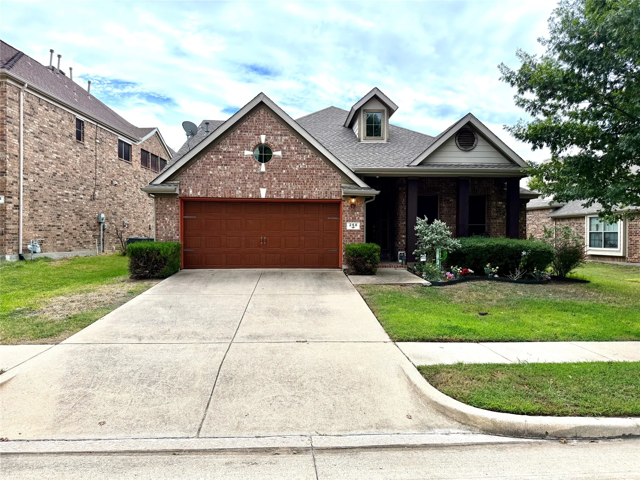 Brick-clad exterior with a prominent dormer window, an attached two-car garage, and a concrete driveway