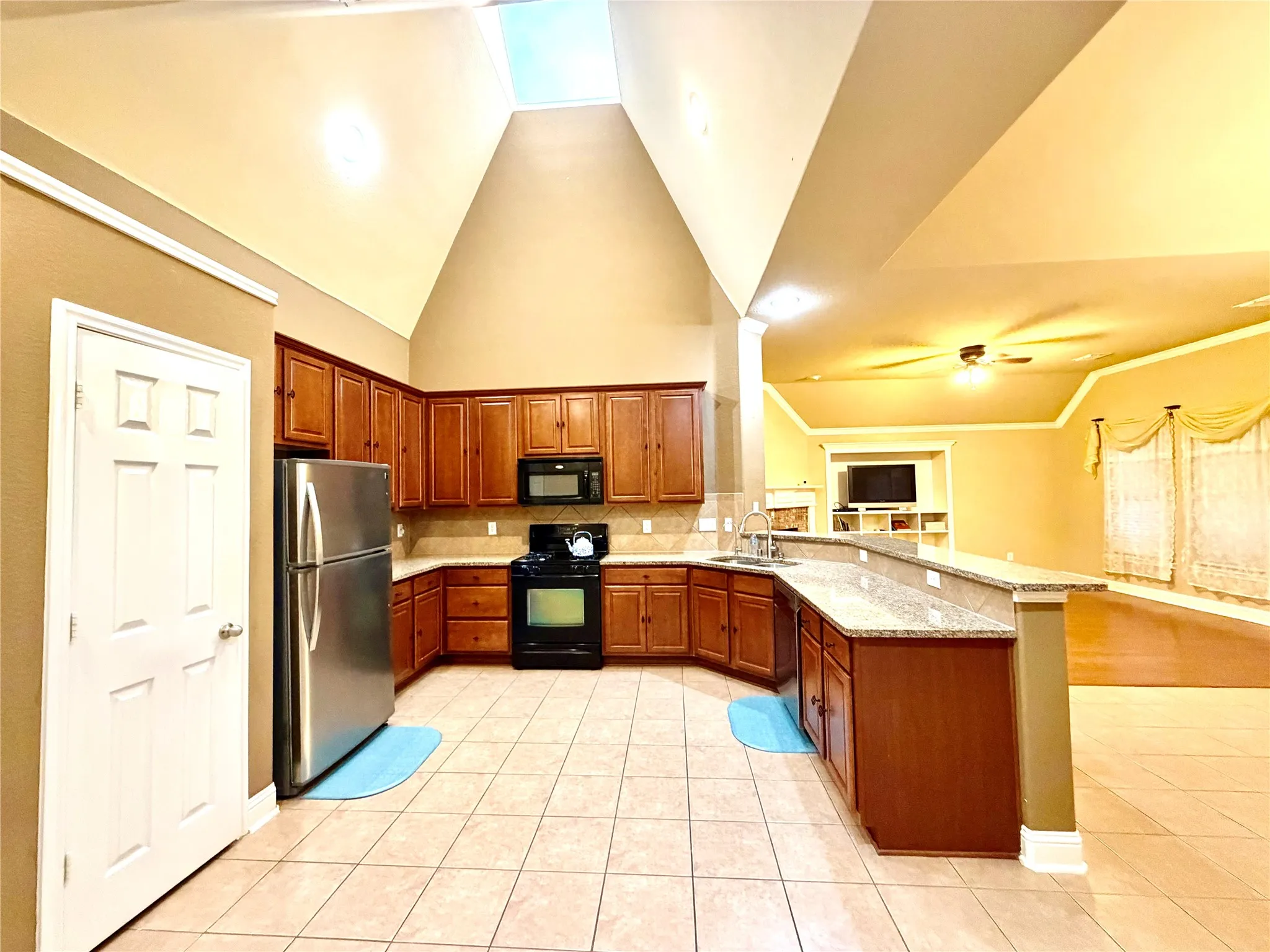 Kitchen featuring vaulted ceilings, a skylight, wood-finish cabinetry, tile flooring, and a breakfast bar
