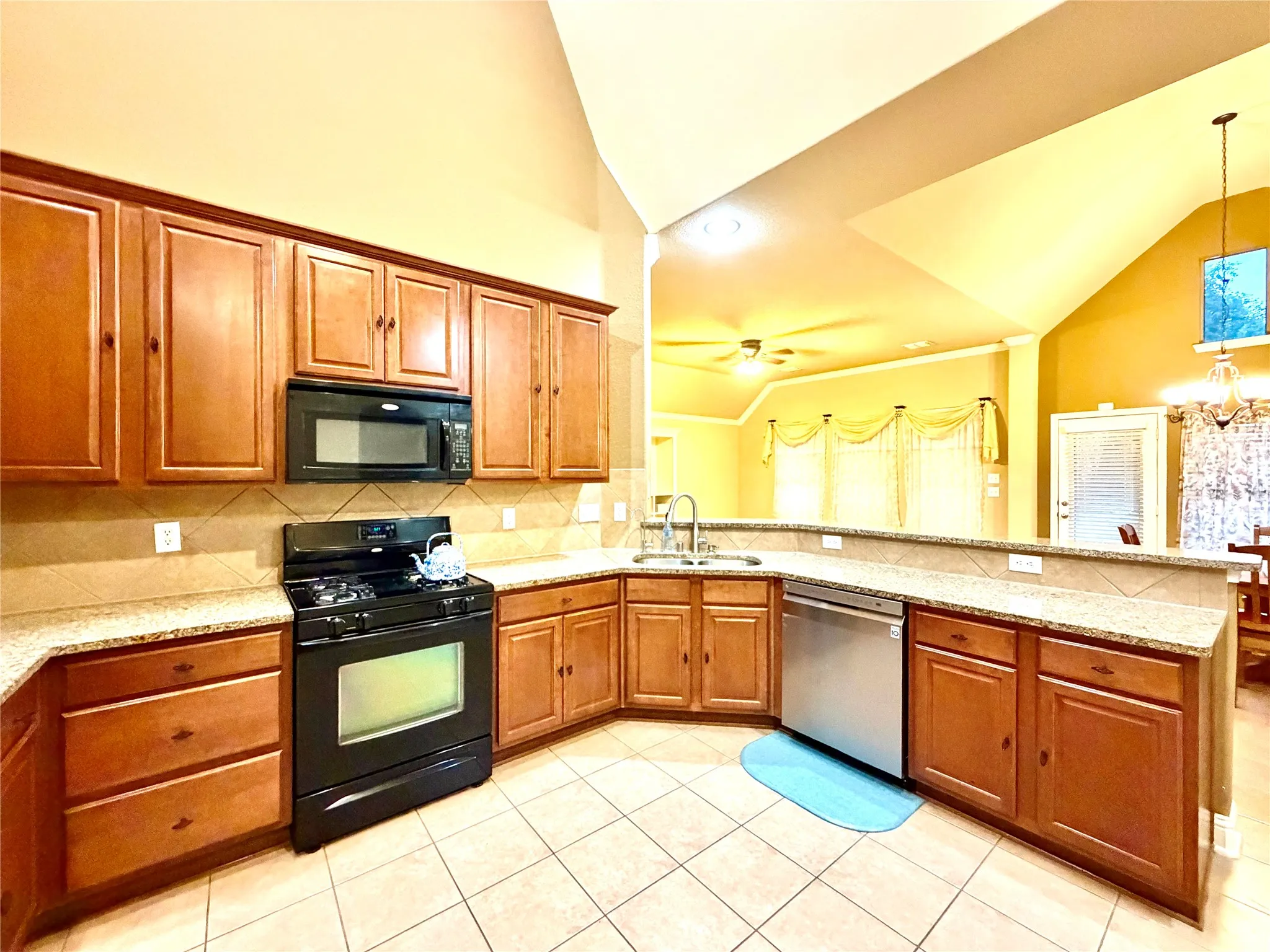 Kitchen featuring wood cabinetry, granite-style countertops, tile flooring, and integrated stainless steel dishwasher