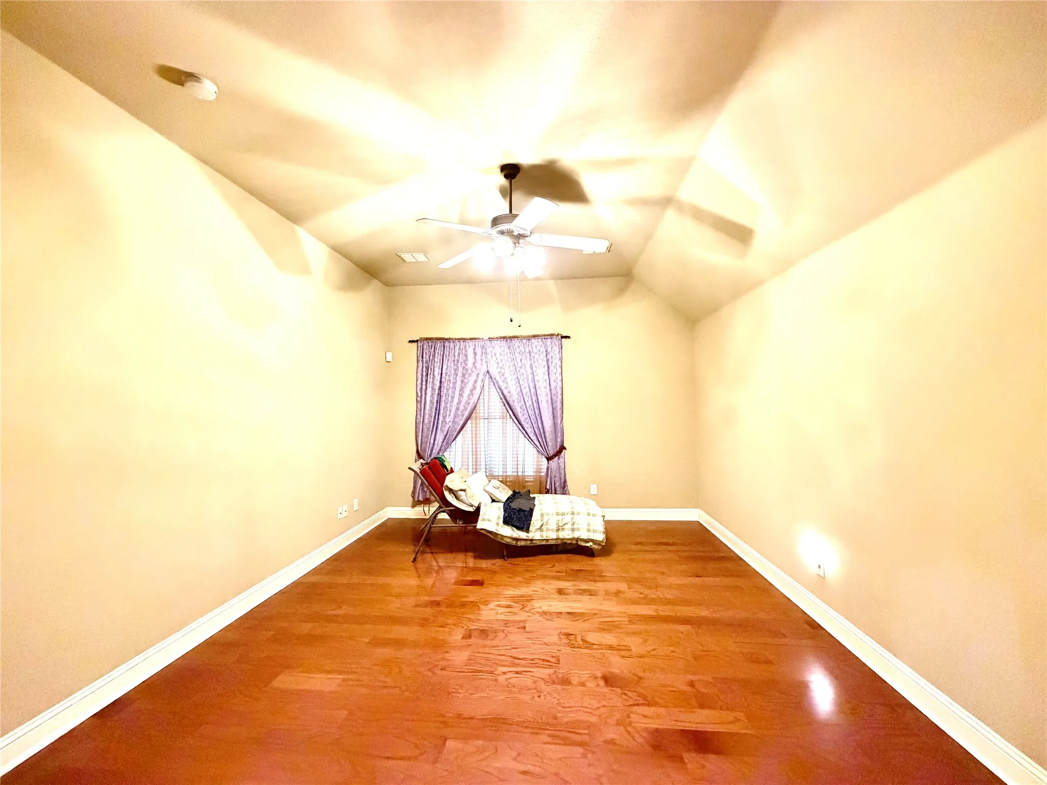 Vaulted ceiling with a ceiling fan, wood-finish flooring, and a window with curtain rod