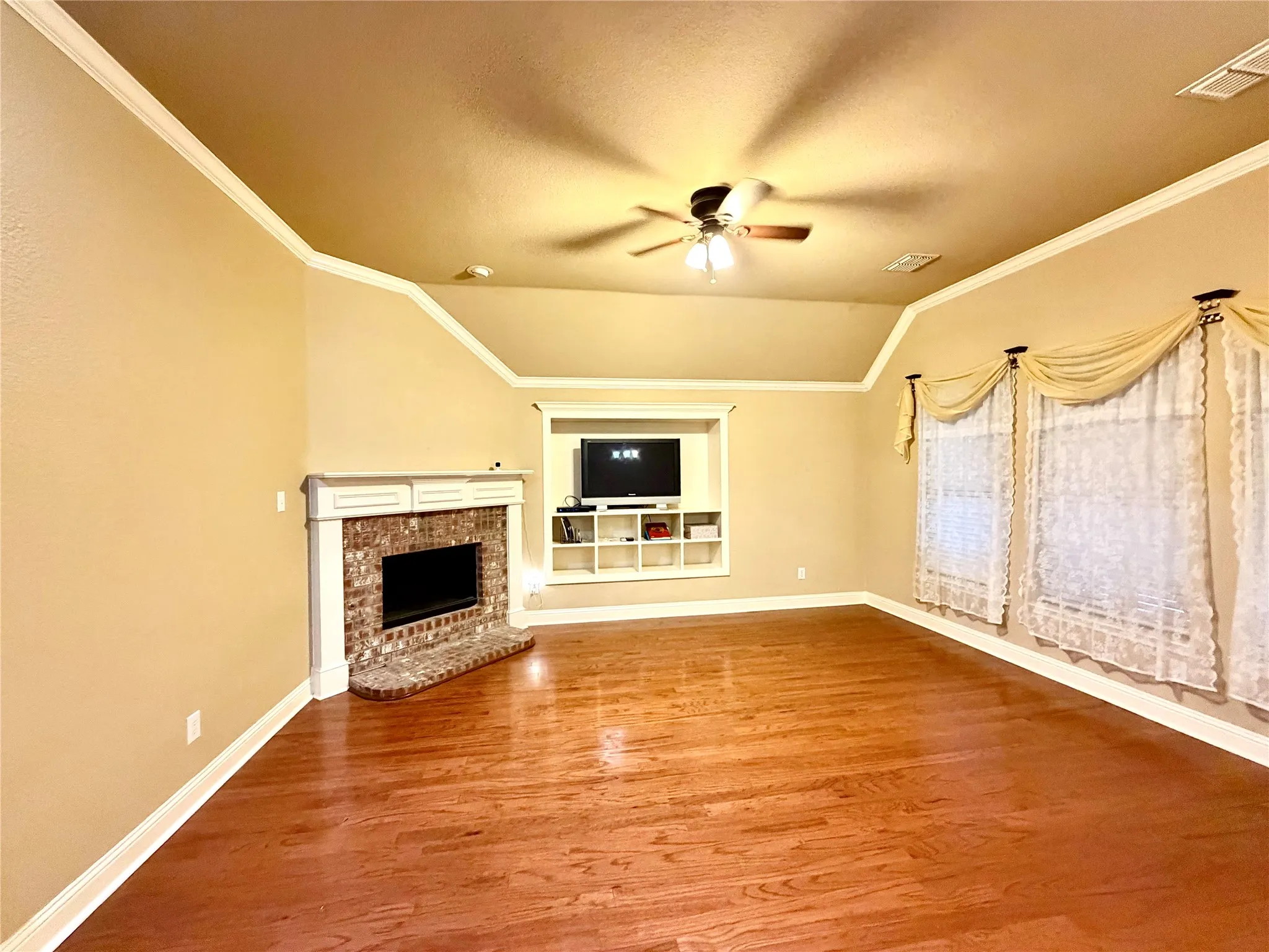 Vaulted ceiling with crown molding, wood-finish flooring, brick fireplace with mantel, and built-in media center