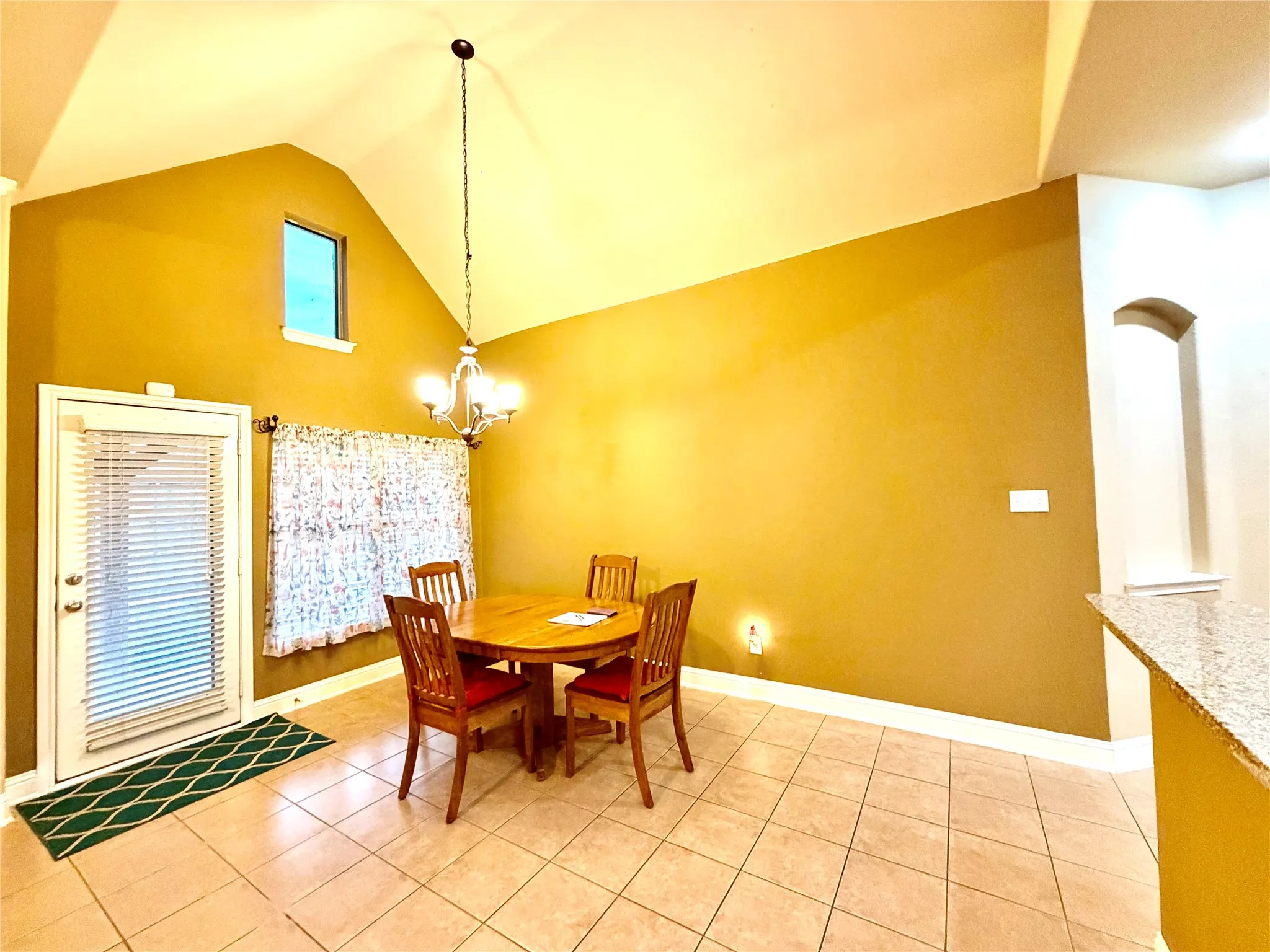 Vaulted ceiling with an architectural accent window, tile flooring, and a chandelier light fixture