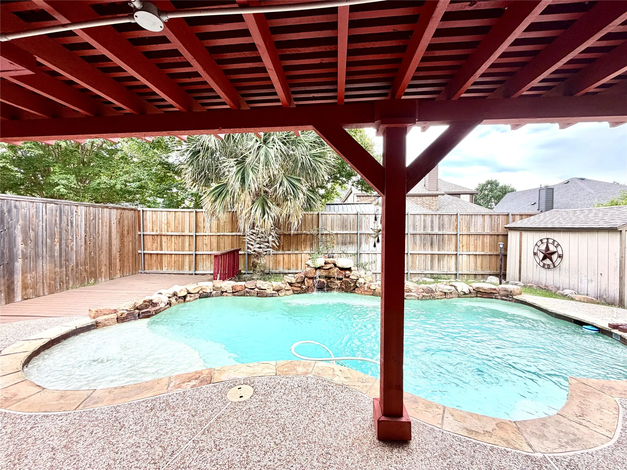 Expansive outdoor living area featuring a pool with rock detailing, a wood deck, and a red-stained covered patio structure