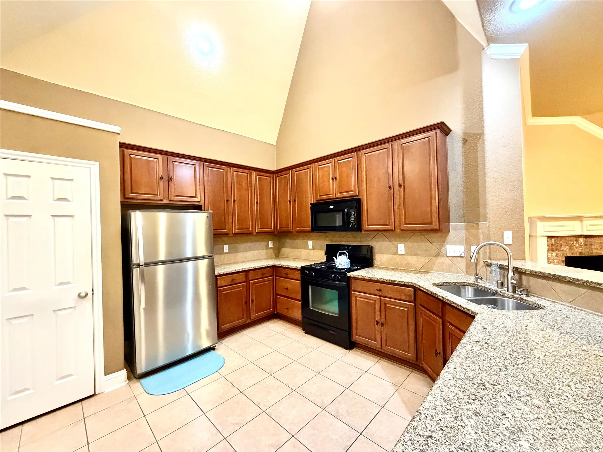 Vaulted ceiling, wood-finish cabinetry, stainless steel refrigerator, black gas range, and a double basin sink