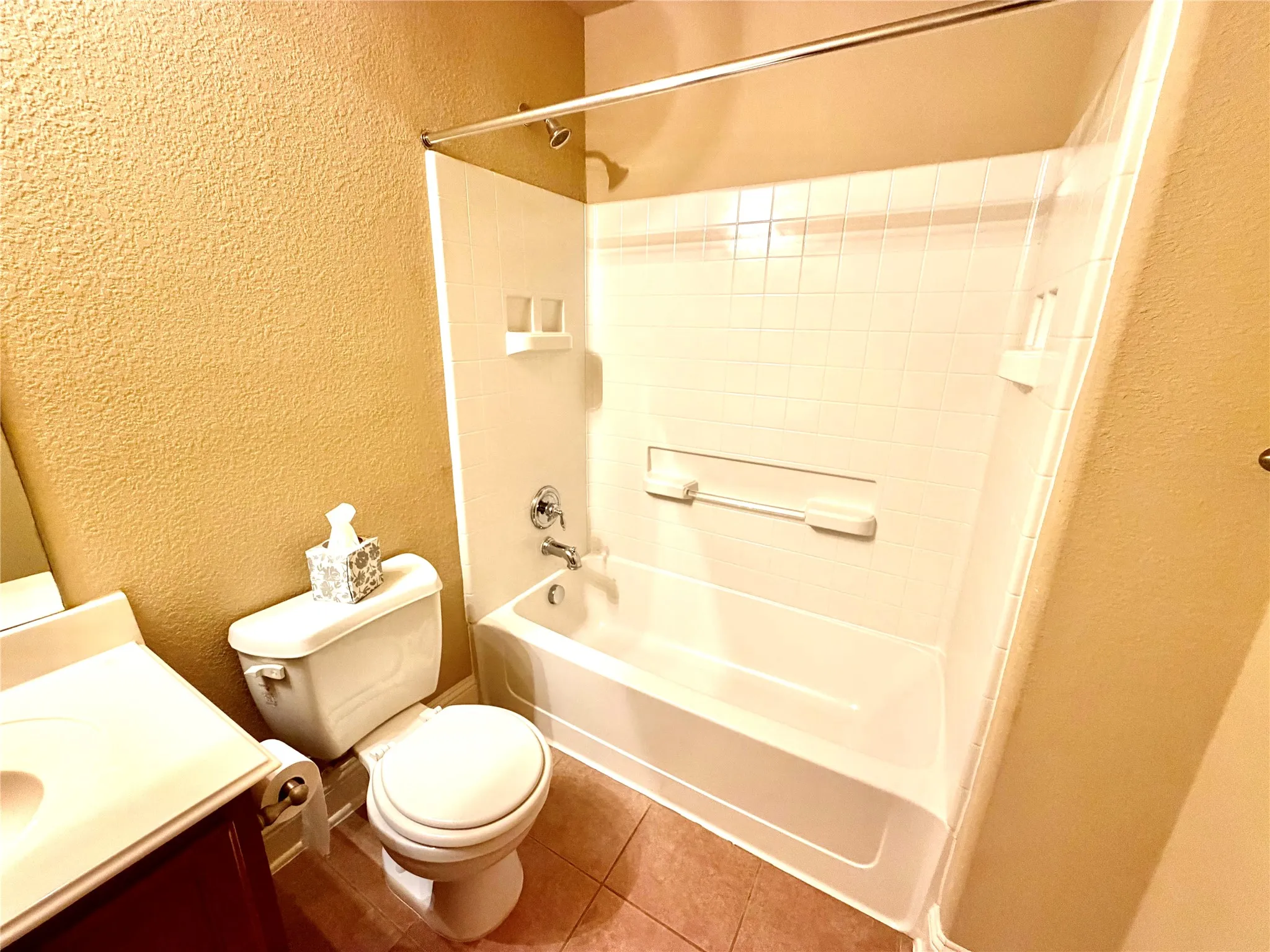 White ceramic tile flooring, built-in bathtub with shower, white commode, and a vanity with an integrated sink