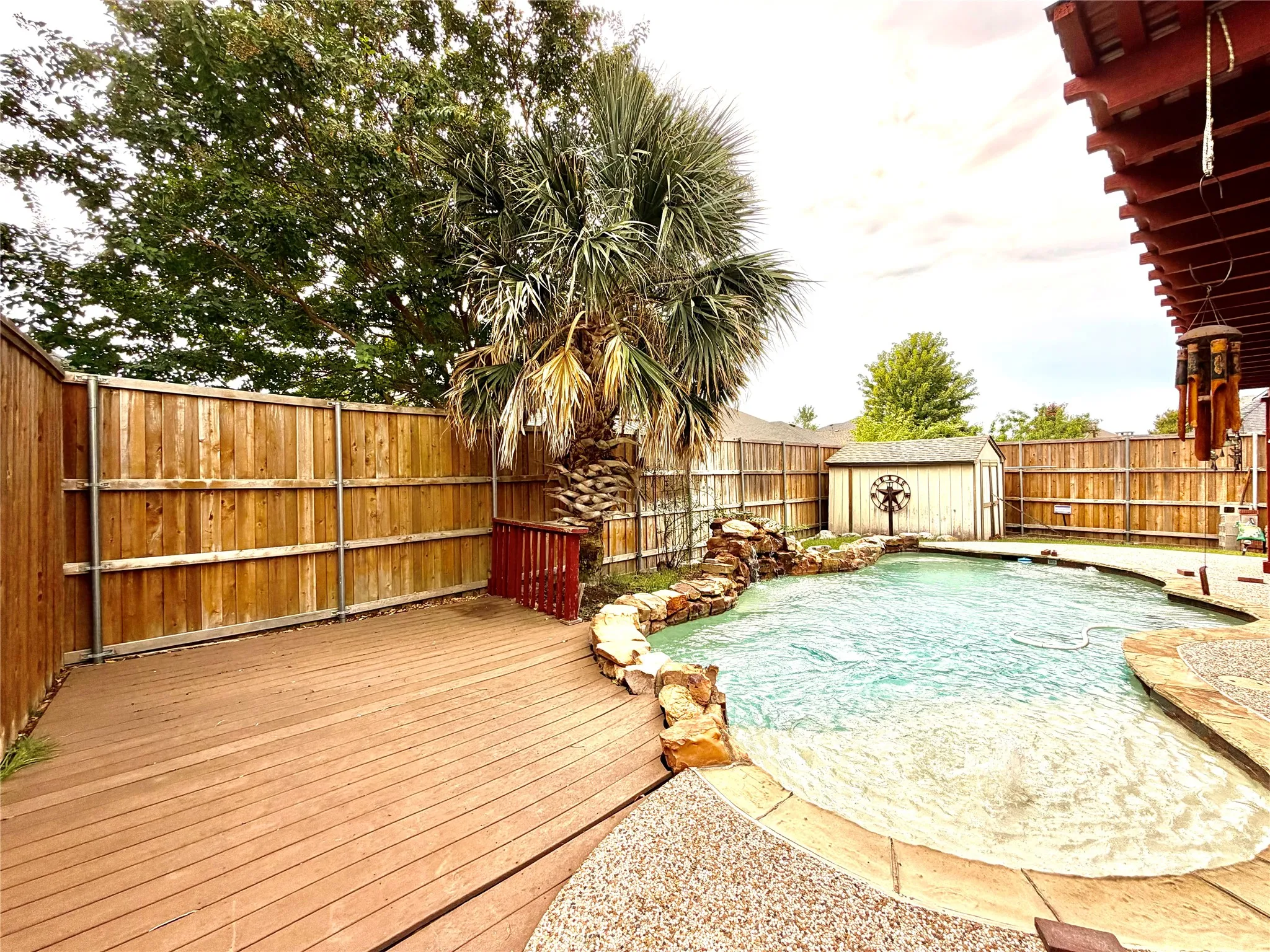 Private backyard featuring a swimming pool with rock waterfall, expansive wood deck, and a storage shed