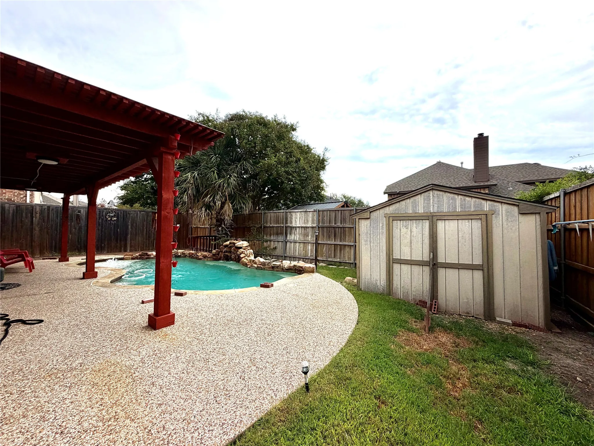 Outdoor living area featuring a covered patio, pebbled aggregate decking, and a built-in swimming pool with a rock waterfall