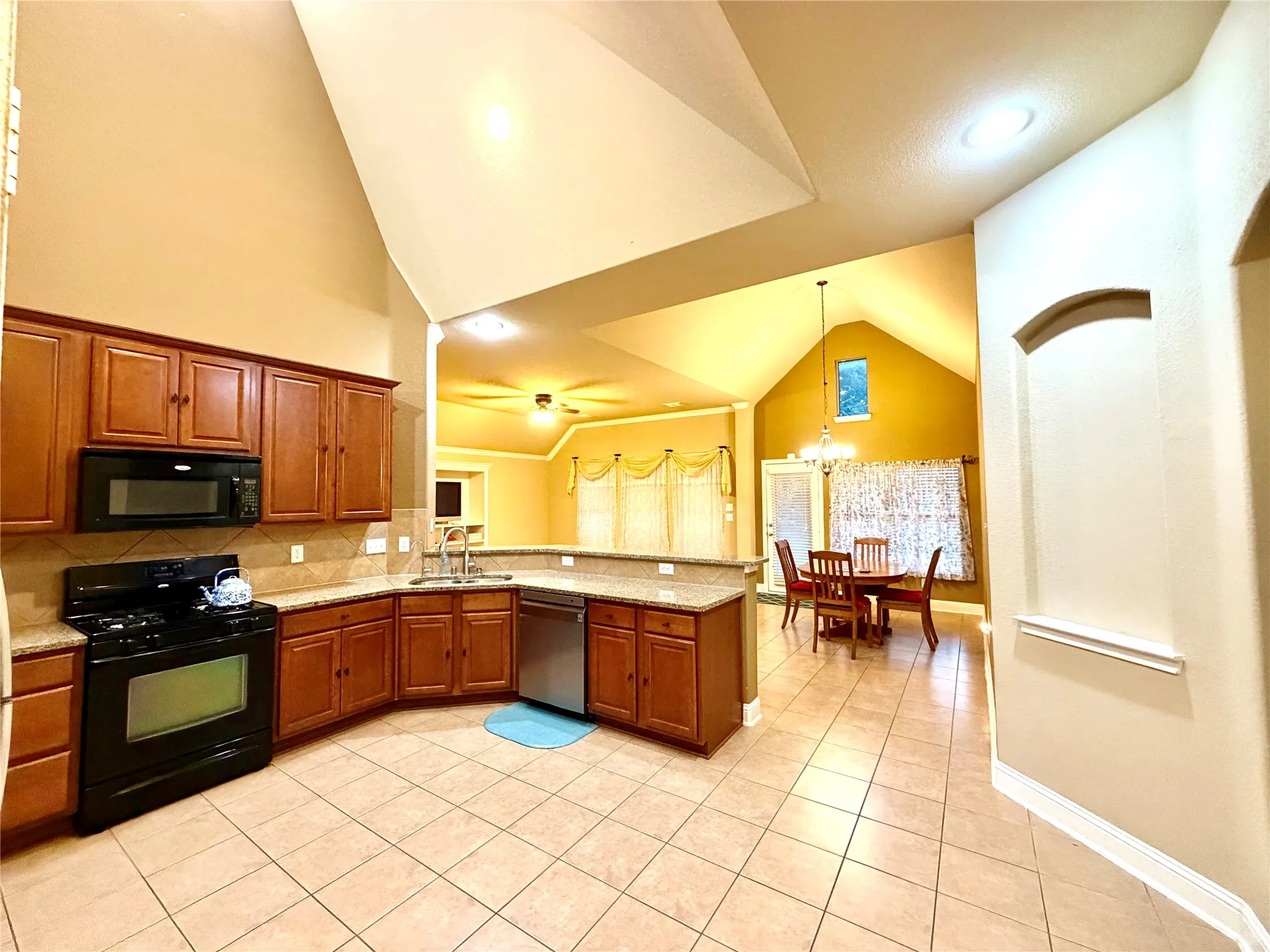 Kitchen featuring wood cabinetry, stone countertops, stainless steel dishwasher, black gas range, and tile flooring