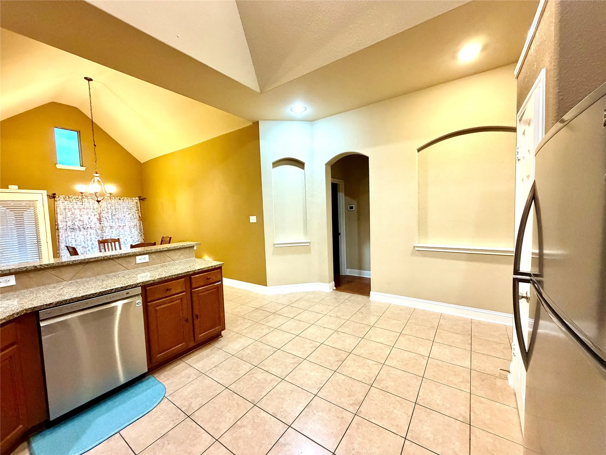 Vaulted ceiling, arched doorways, tiled flooring, wood-finish cabinetry, and stainless steel dishwasher