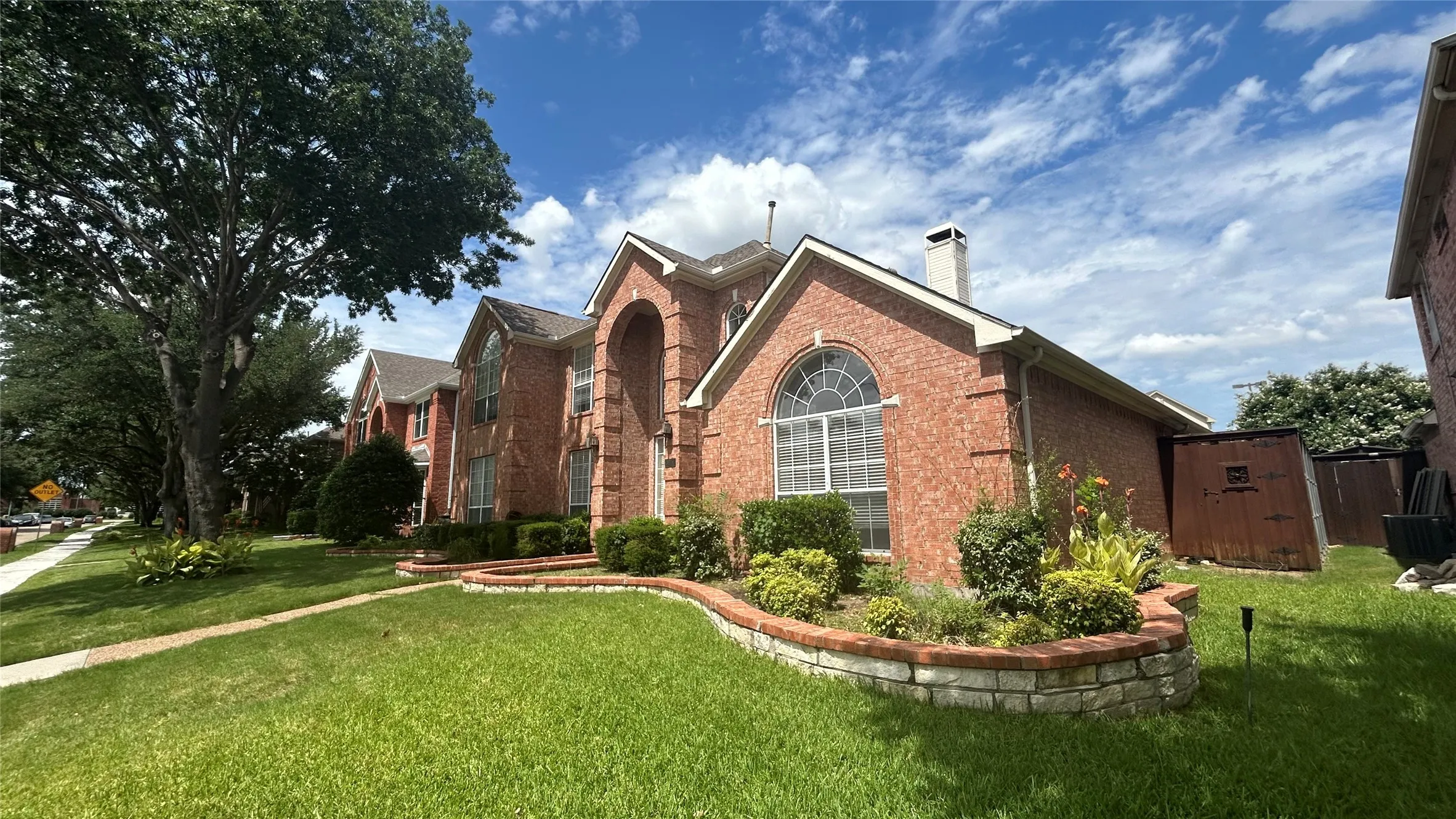 Brick exterior with arched entry, arched window, chimney, and landscaped garden beds with stone and brick retaining walls