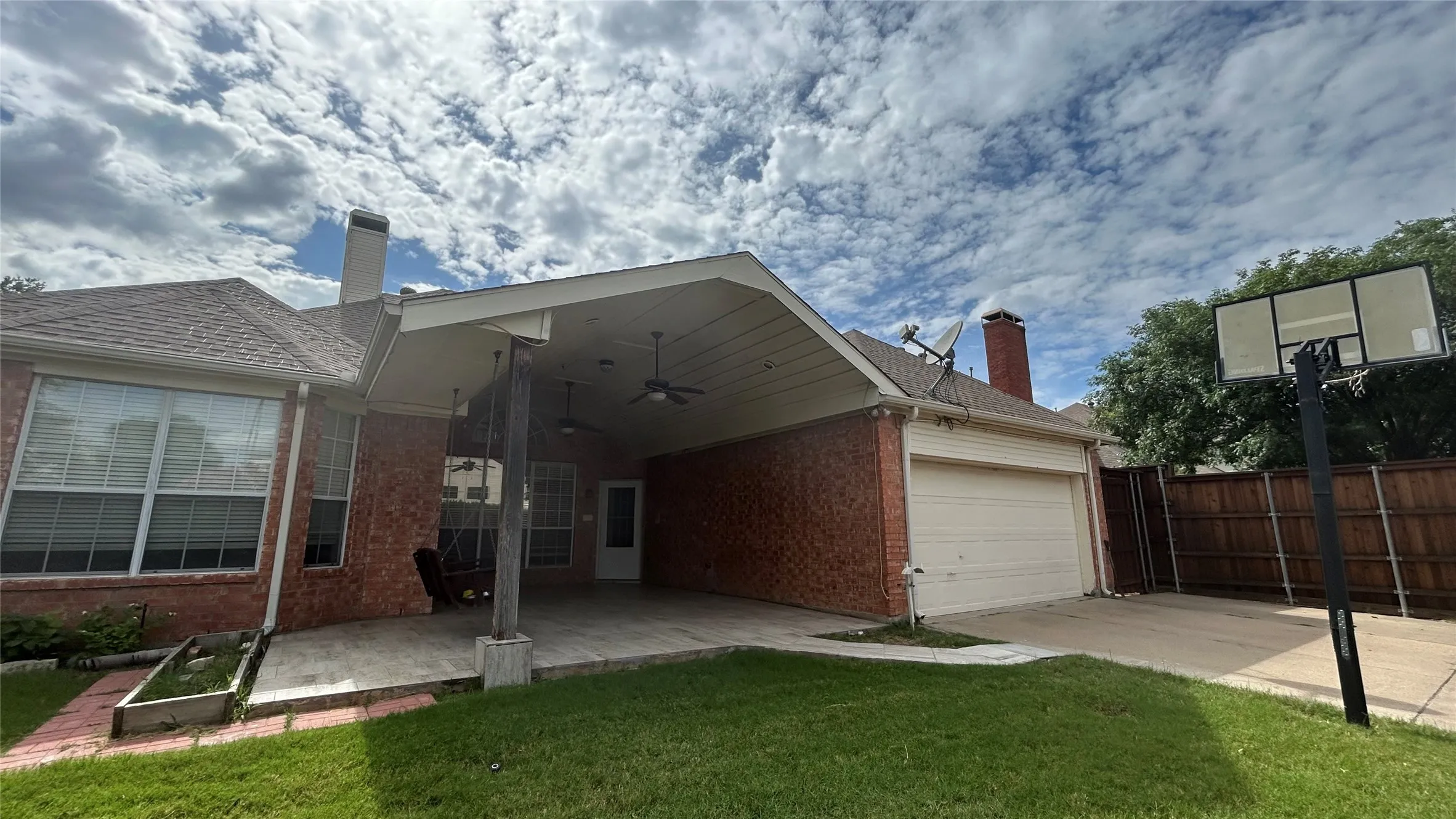 Brick exterior with a covered patio featuring ceiling fans, a concrete patio, and a two-car garage with a driveway