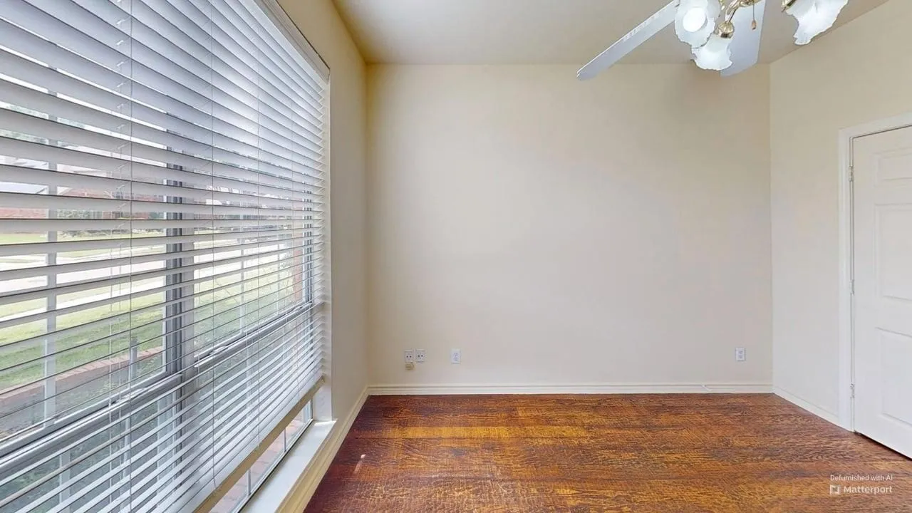 Spacious room featuring wood-finish flooring, a large window with blinds, a ceiling fan with integrated lighting, and a paneled door
