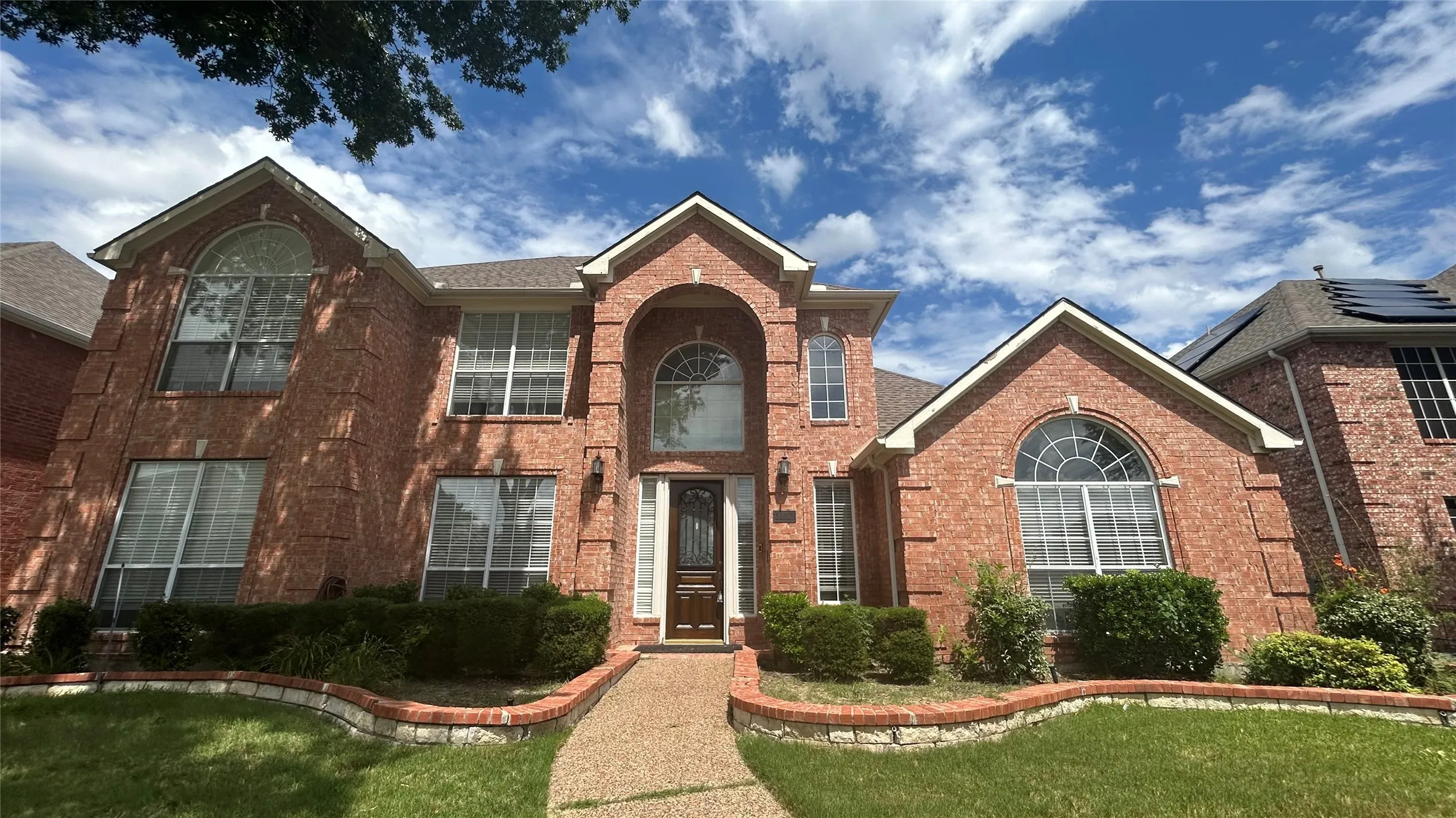 Two-story brick exterior with arched windows, a covered entry, gabled rooflines, and manicured landscaping