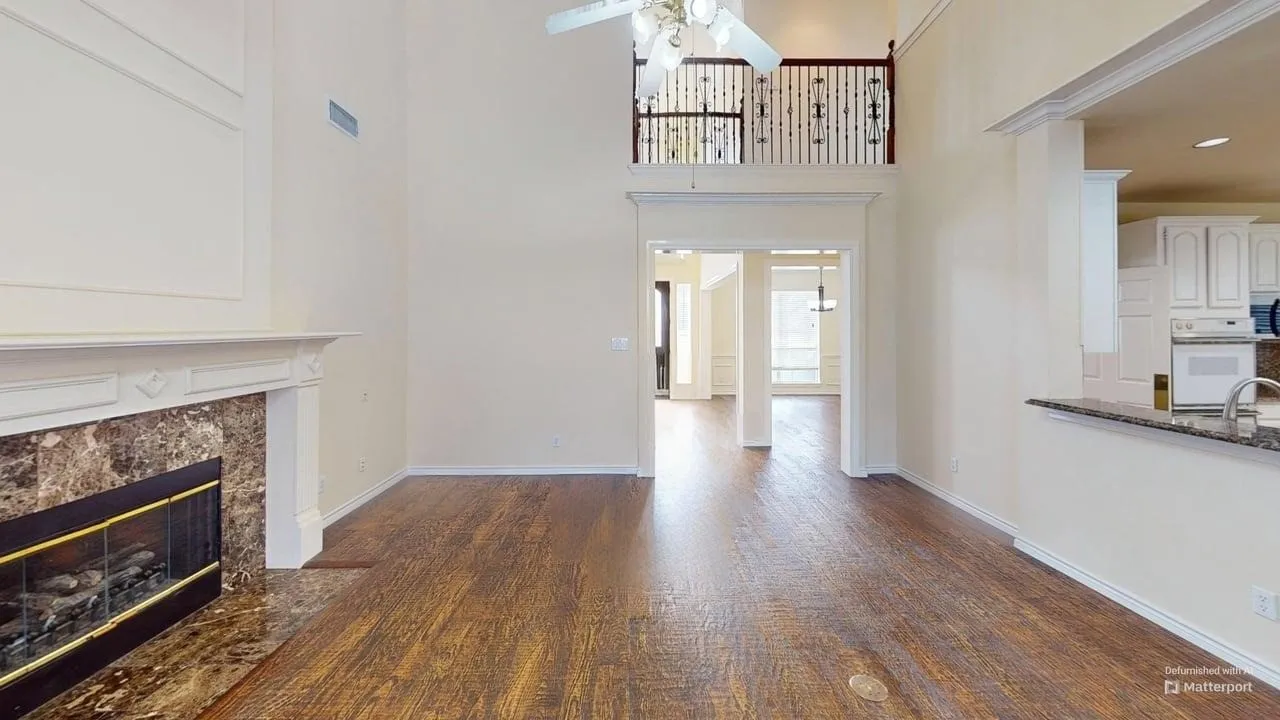 Two-story living area featuring wood-finish flooring, a fireplace with a stone surround, and an upper-level balcony with decorative railings