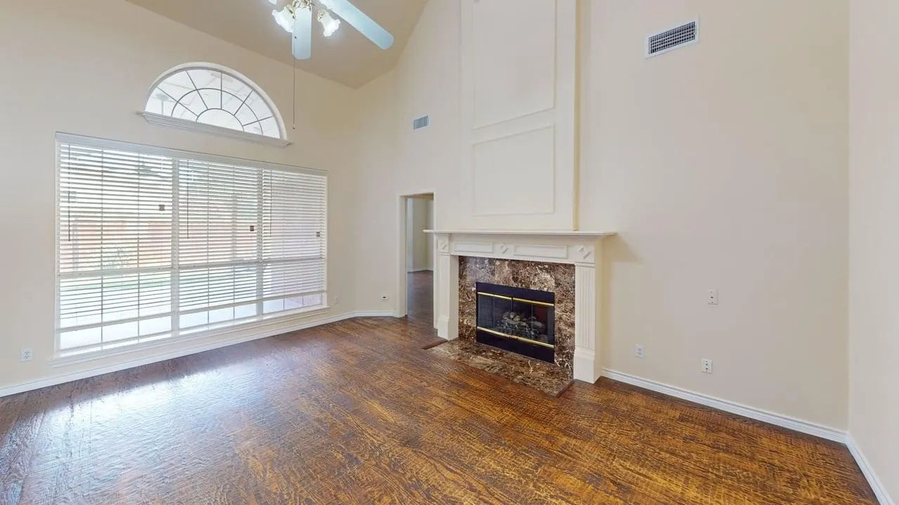 Vaulted ceiling, wood-finish flooring, large window with arch transom, fireplace with stone surround, and decorative wall paneling