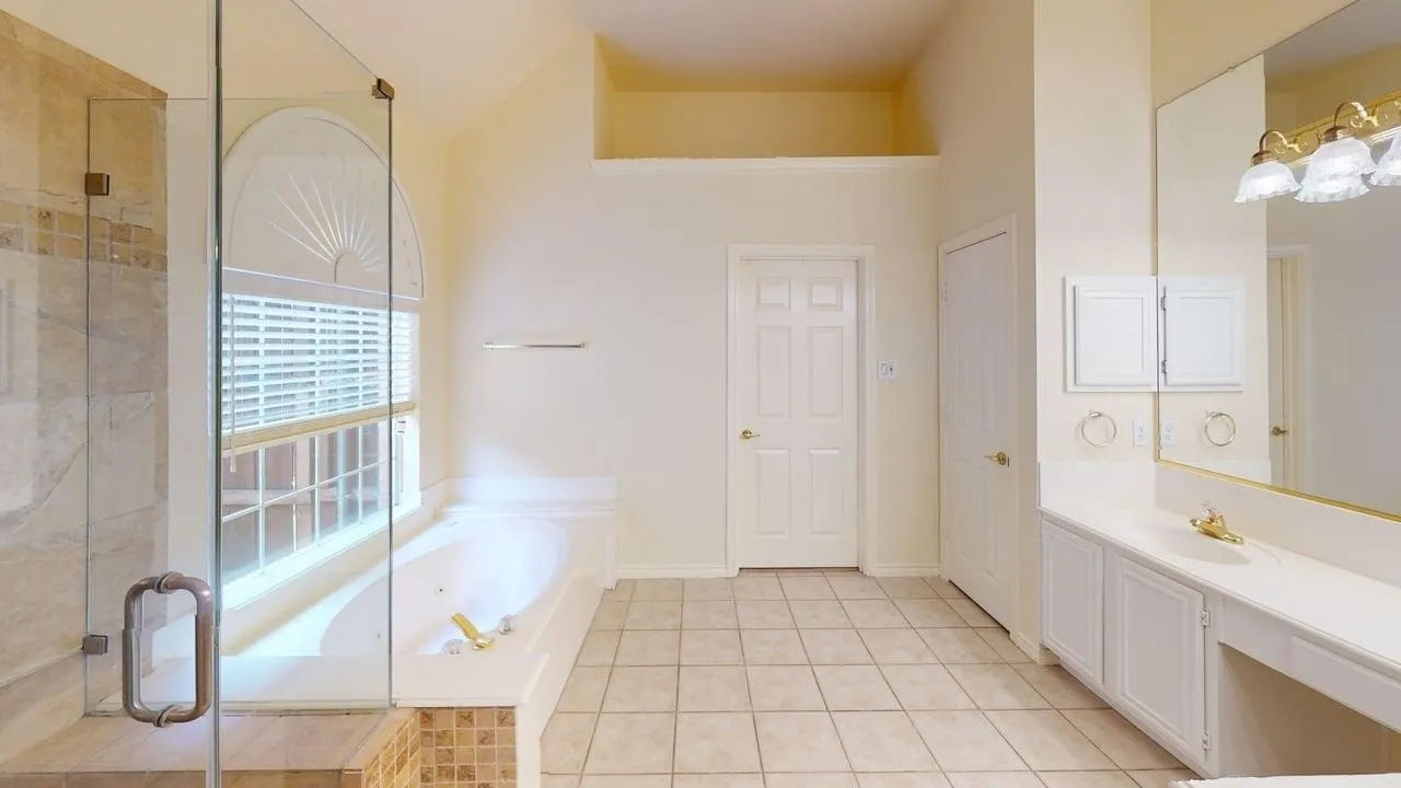 Spacious bathroom featuring a built-in soaking tub, glass-enclosed shower with tile surround, dual vanity with integrated sink, and large wall-mounted mirror