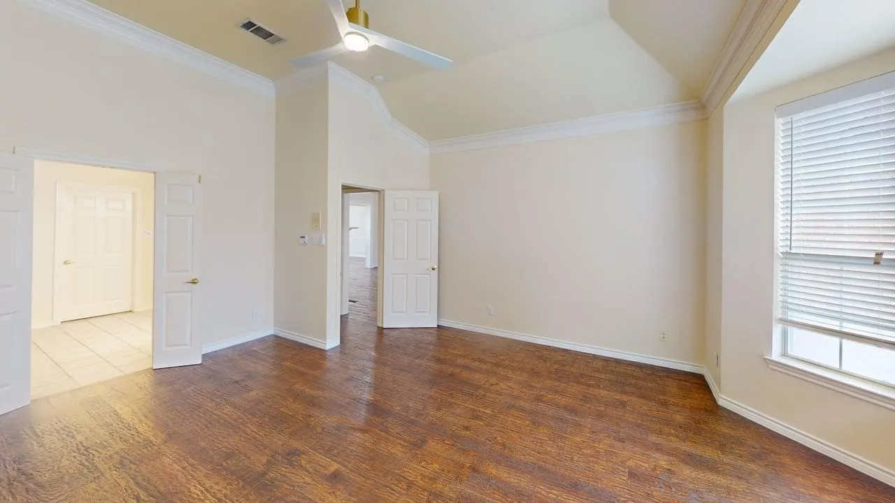 Wood-finish flooring, vaulted ceiling with crown molding, ceiling fan, and bay window