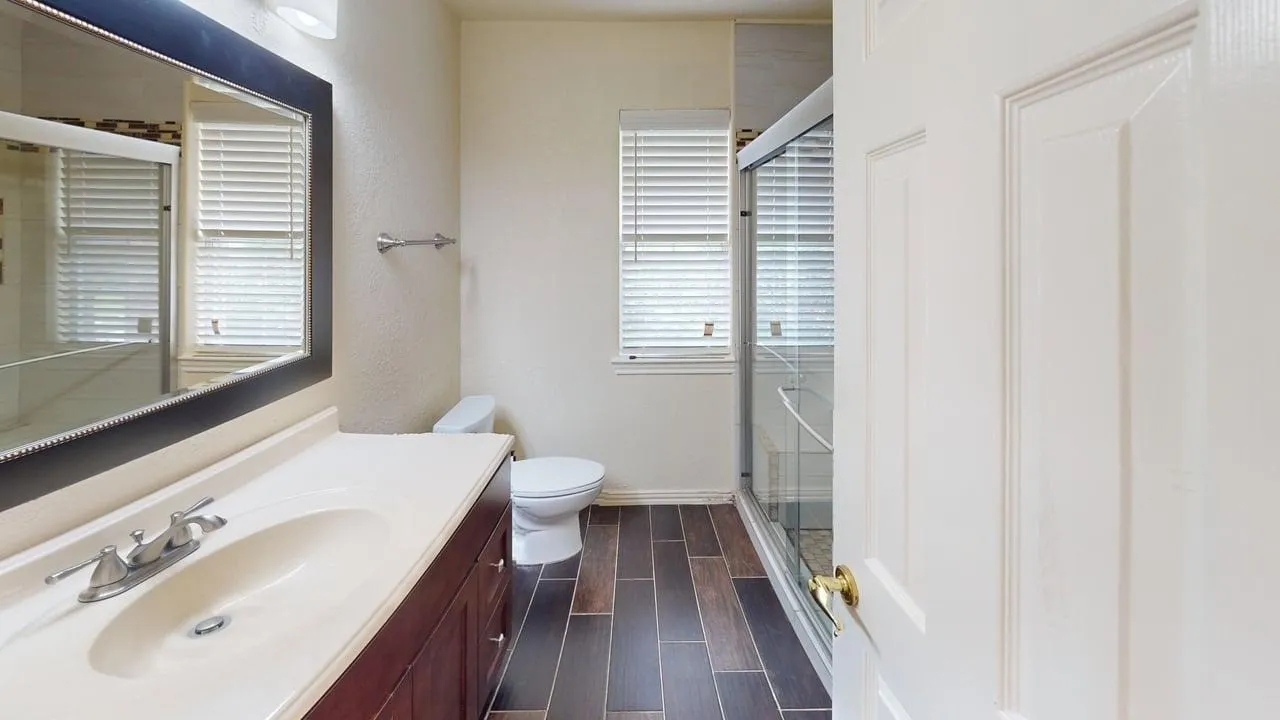 Vanity with integrated sink, framed mirror, wood-finish flooring, and glass-enclosed shower