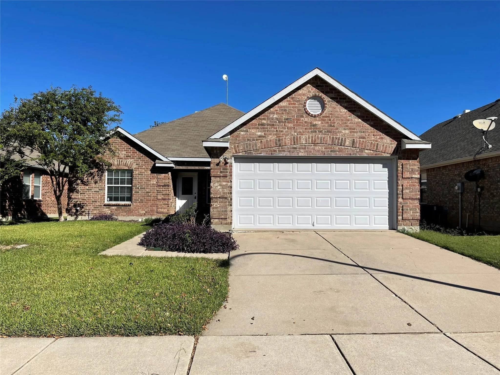 Brick exterior, attached garage, concrete driveway, mature tree, and landscaped planting beds