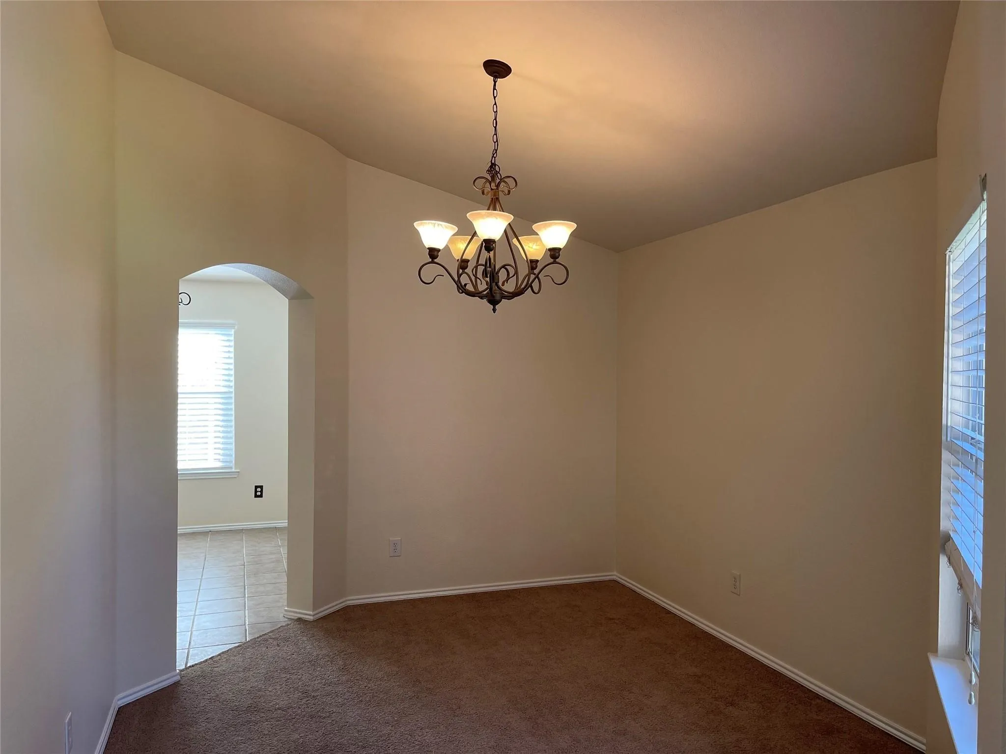 Vaulted ceiling with an ornate chandelier, arched doorway, and window with blinds