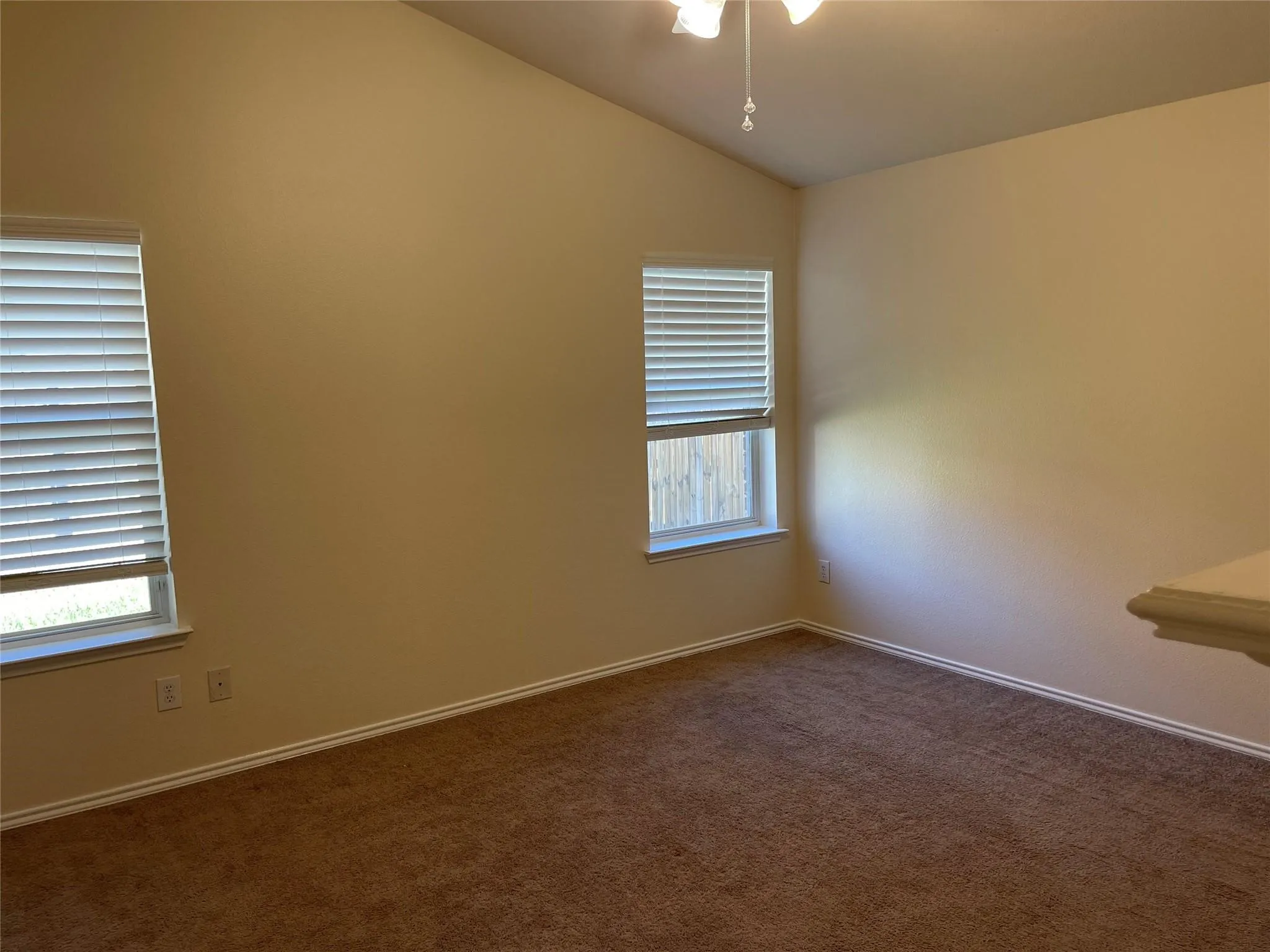 Vaulted ceiling with a ceiling fan, dual windows with blinds, and brown carpeting