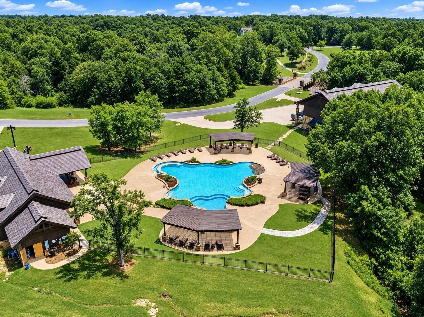 Resort-style pool with surrounding lounge areas, expansive manicured lawn, paved walkways, and mature trees