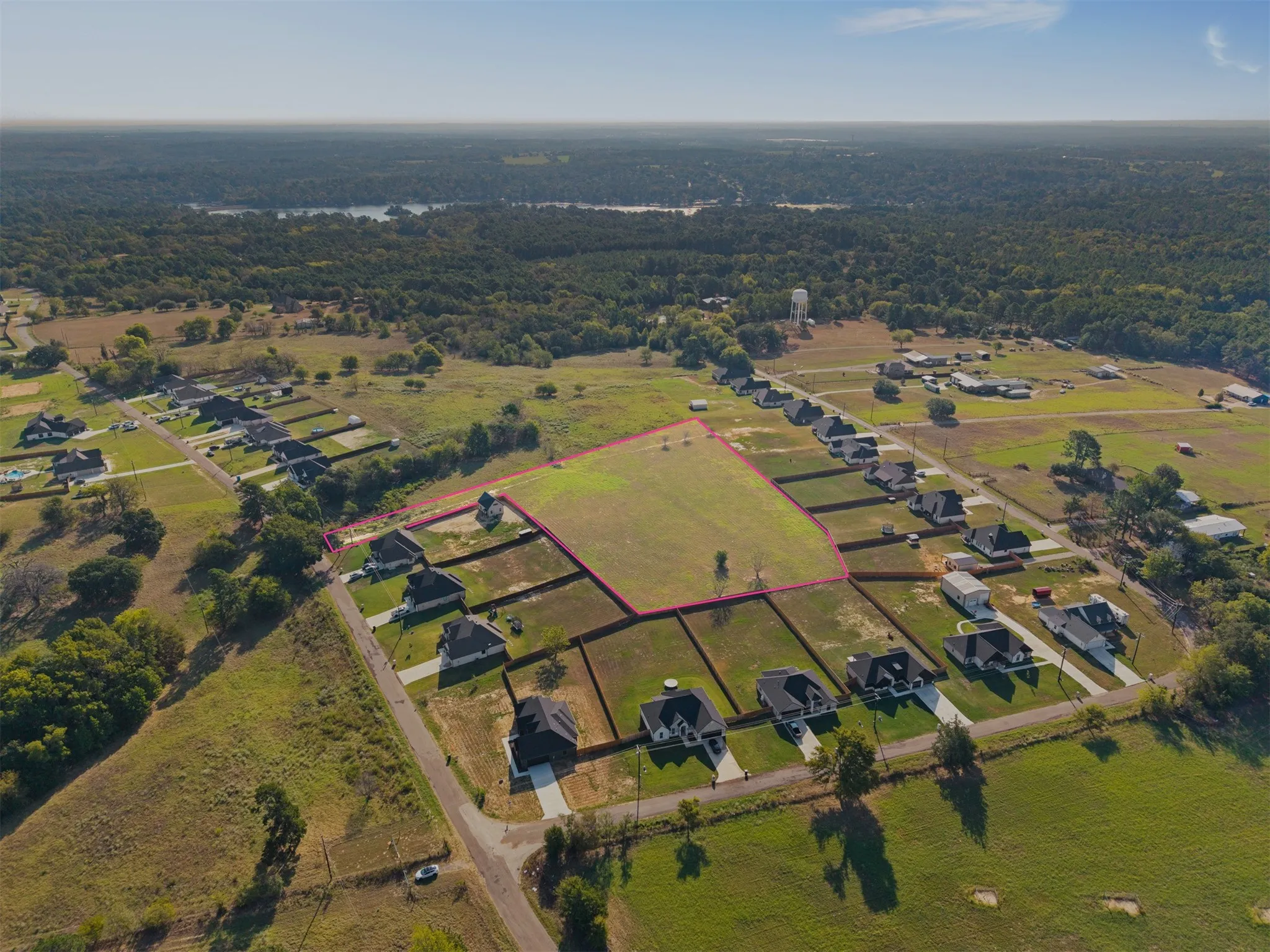 Expansive land parcel featuring clear, undeveloped terrain within a residential area, surrounded by established properties, with distant water visible