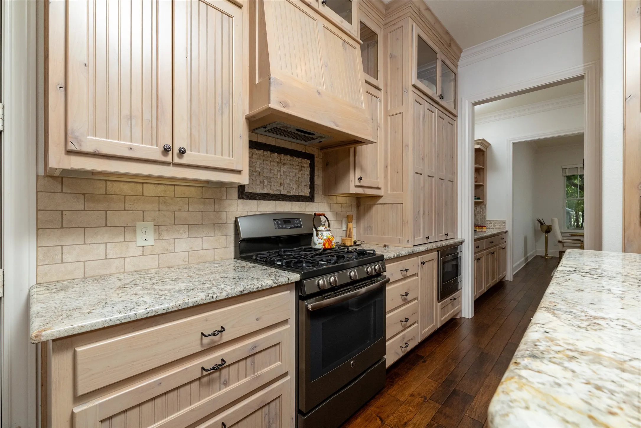 Light-toned wood cabinetry with glass-front accents, subway tile backsplash, granite-finish countertops, and dark wood-finish flooring