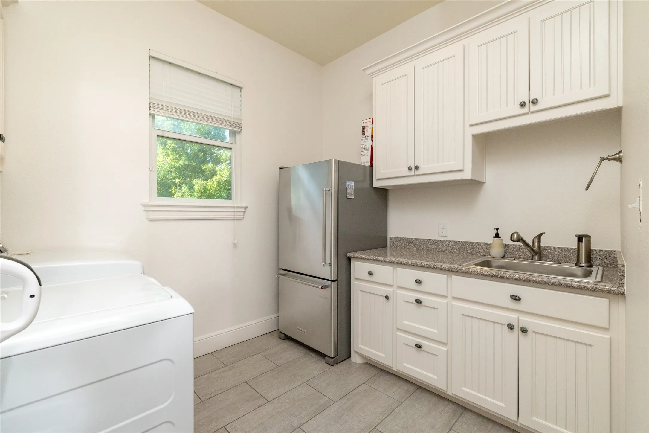 White cabinetry, undermount sink, stone-finish countertop, tiled flooring, and a single window