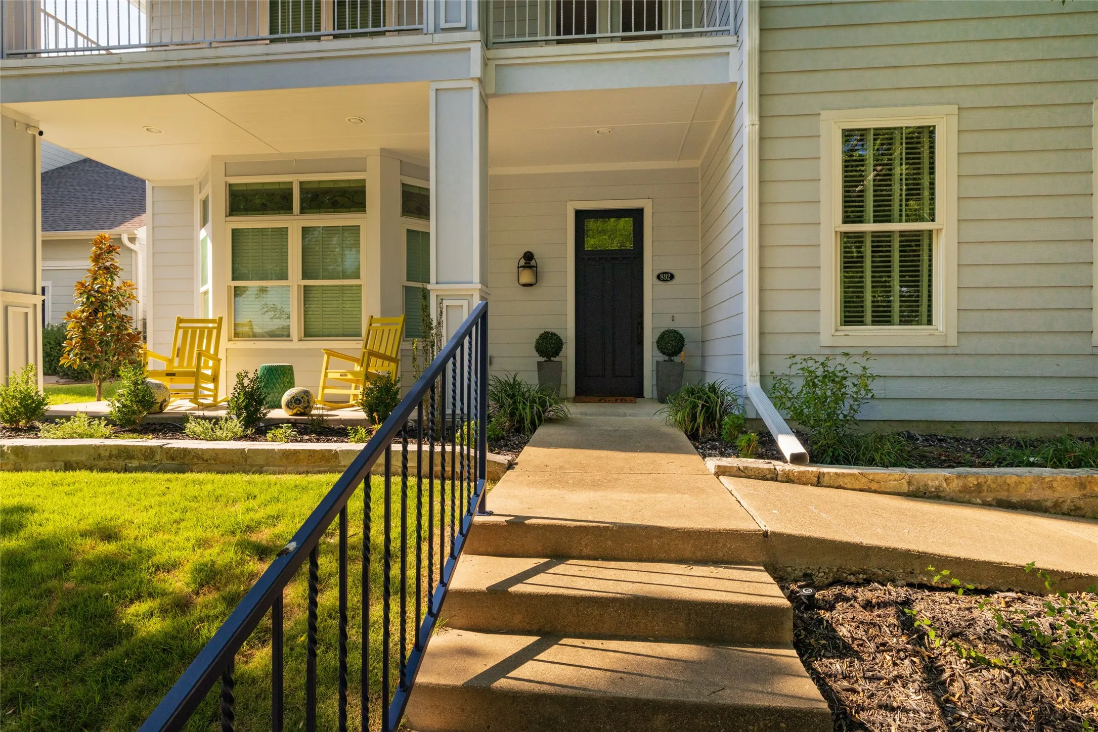 Light blue siding exterior featuring a covered porch, bay window, dark entry door, and wrought iron handrail