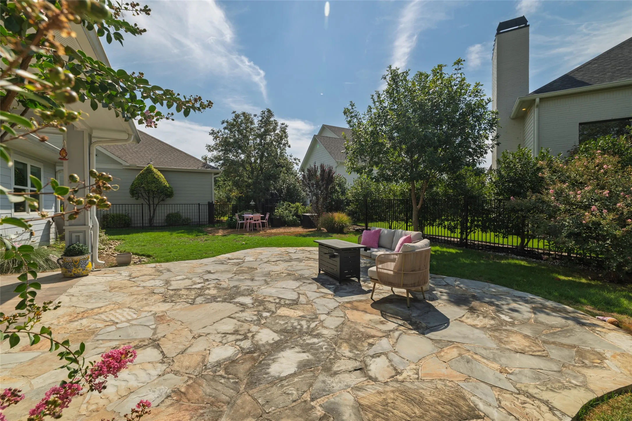Expansive flagstone patio with a manicured lawn, established trees, and perimeter fencing