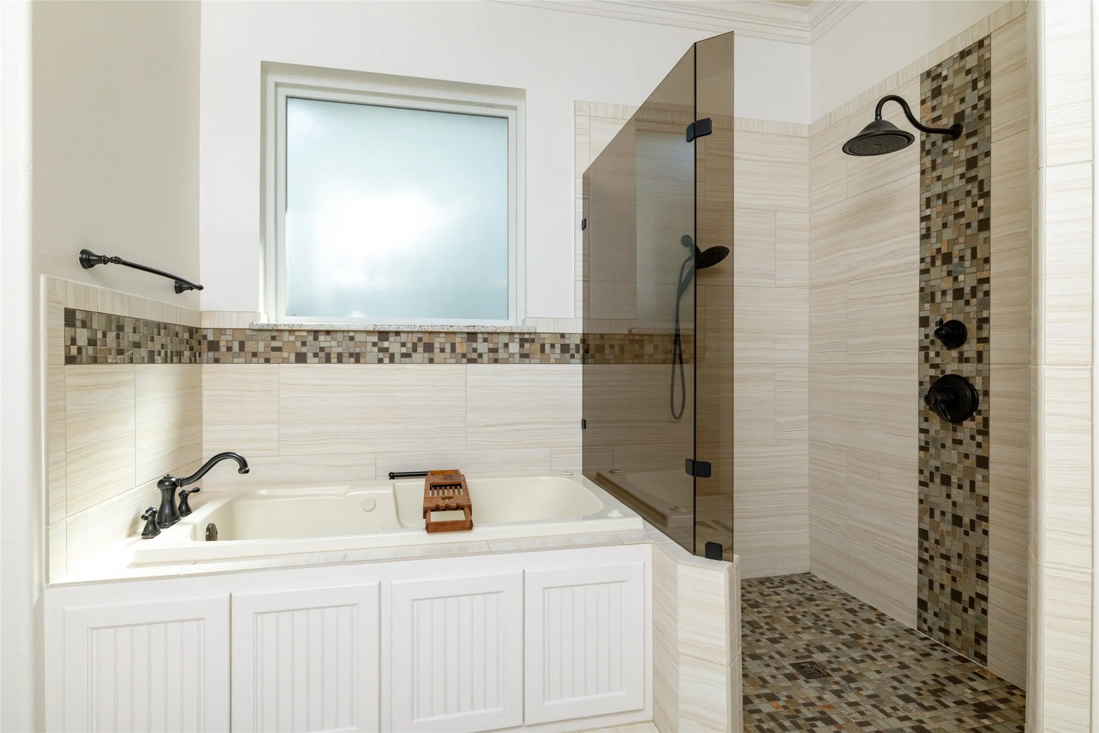 Built-in soaking tub with beadboard cabinetry, walk-in shower with fixed glass panel, mosaic tile accents, and matte black fixtures