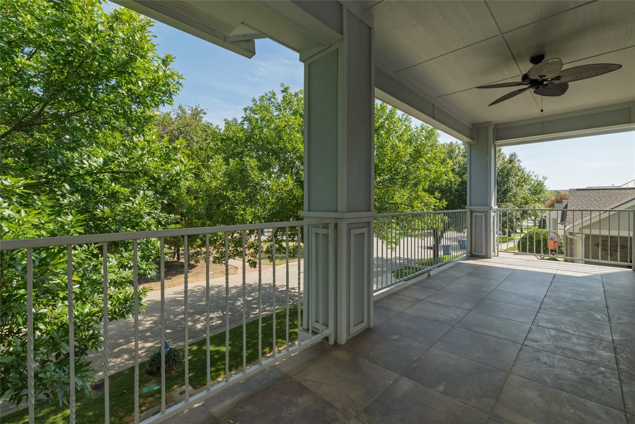 Expansive covered balcony featuring a ceiling fan, tiled flooring, painted columns, and a metal railing