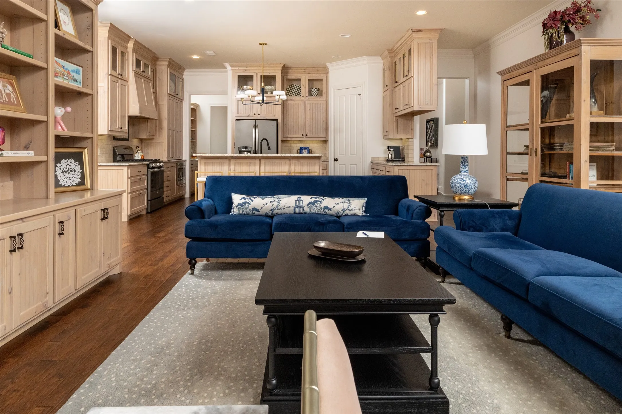 Open concept living area with wood-finish flooring, light-toned custom cabinetry, stainless steel appliances, and built-in shelving