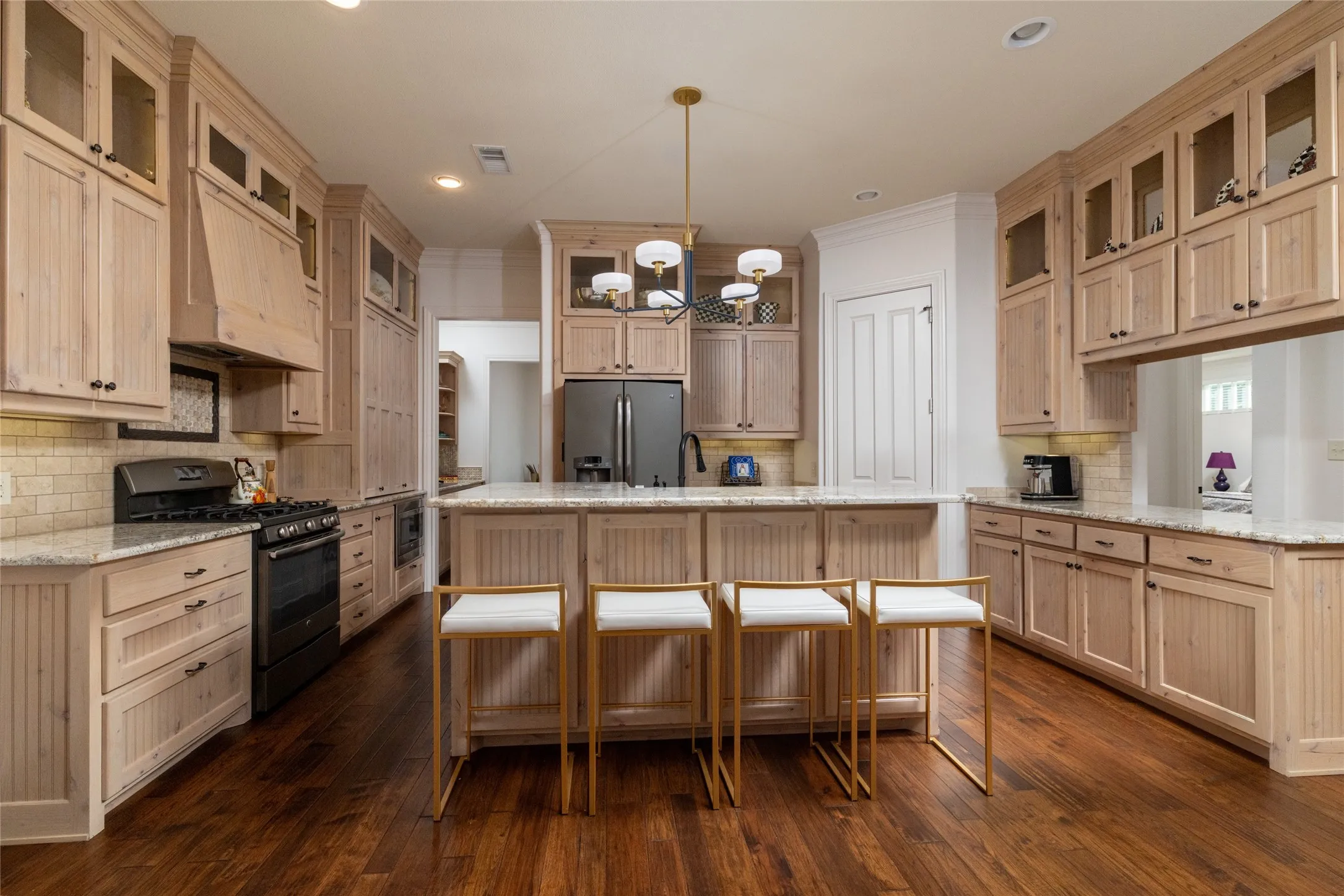 Wood-finish flooring, light wood cabinetry, stone countertops, integrated range, and a central island with pendant lighting