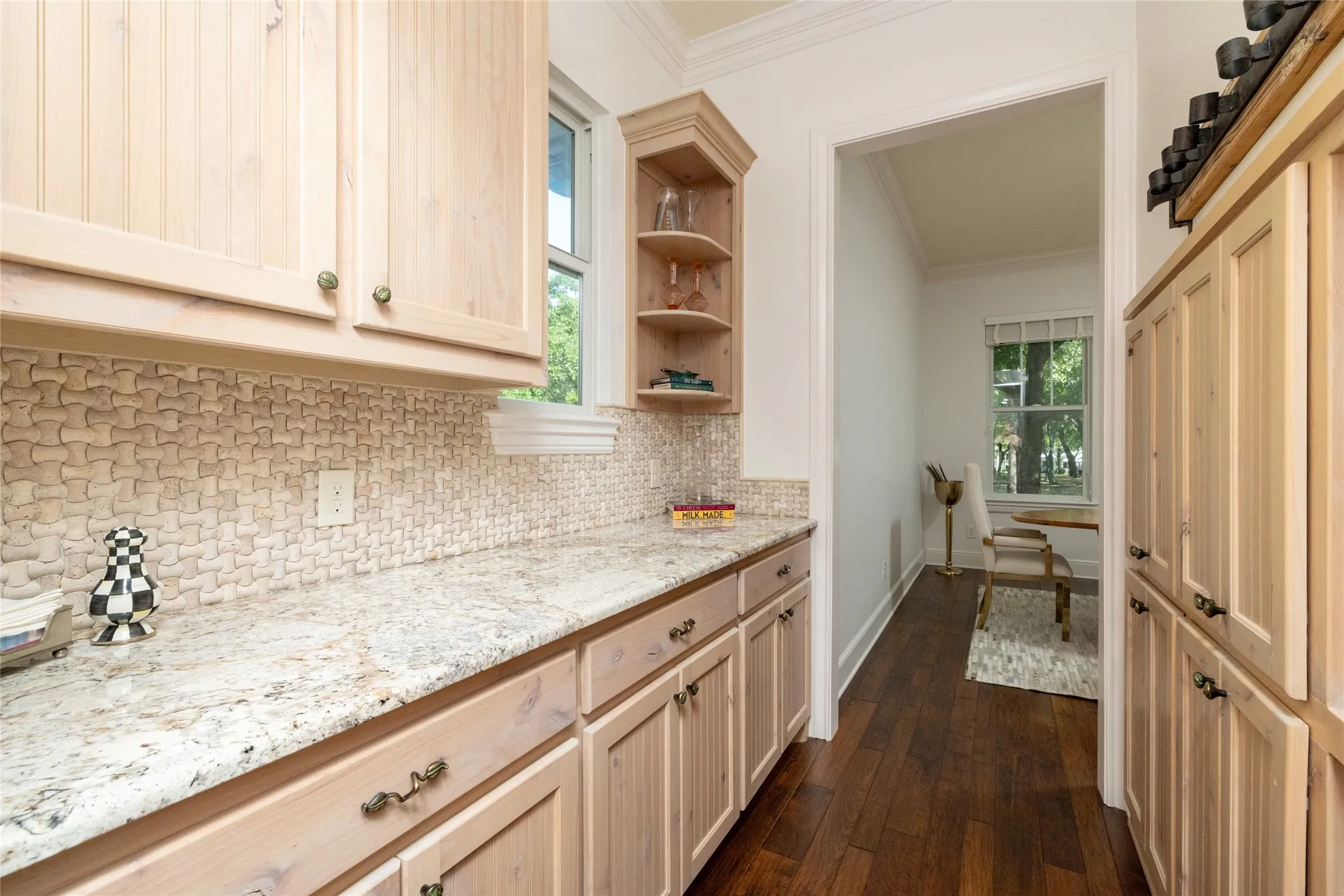 Light wood cabinetry with brass-toned hardware, stone-finish countertops, mosaic tile backsplash, and dark wood-finish flooring
