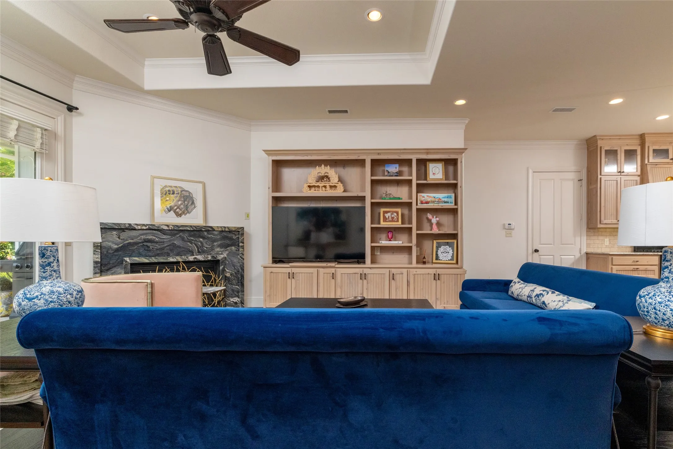 Tray ceiling with a ceiling fan, built-in entertainment center, black stone fireplace surround, and recessed lighting