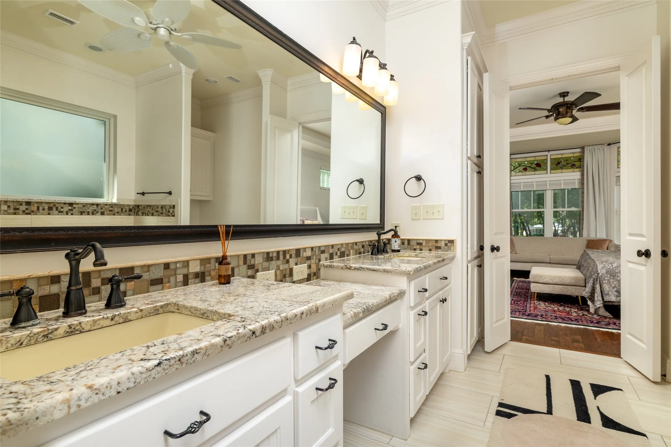 Double vanity with granite countertops, integrated sinks, white cabinetry, and a mosaic tile backsplash
