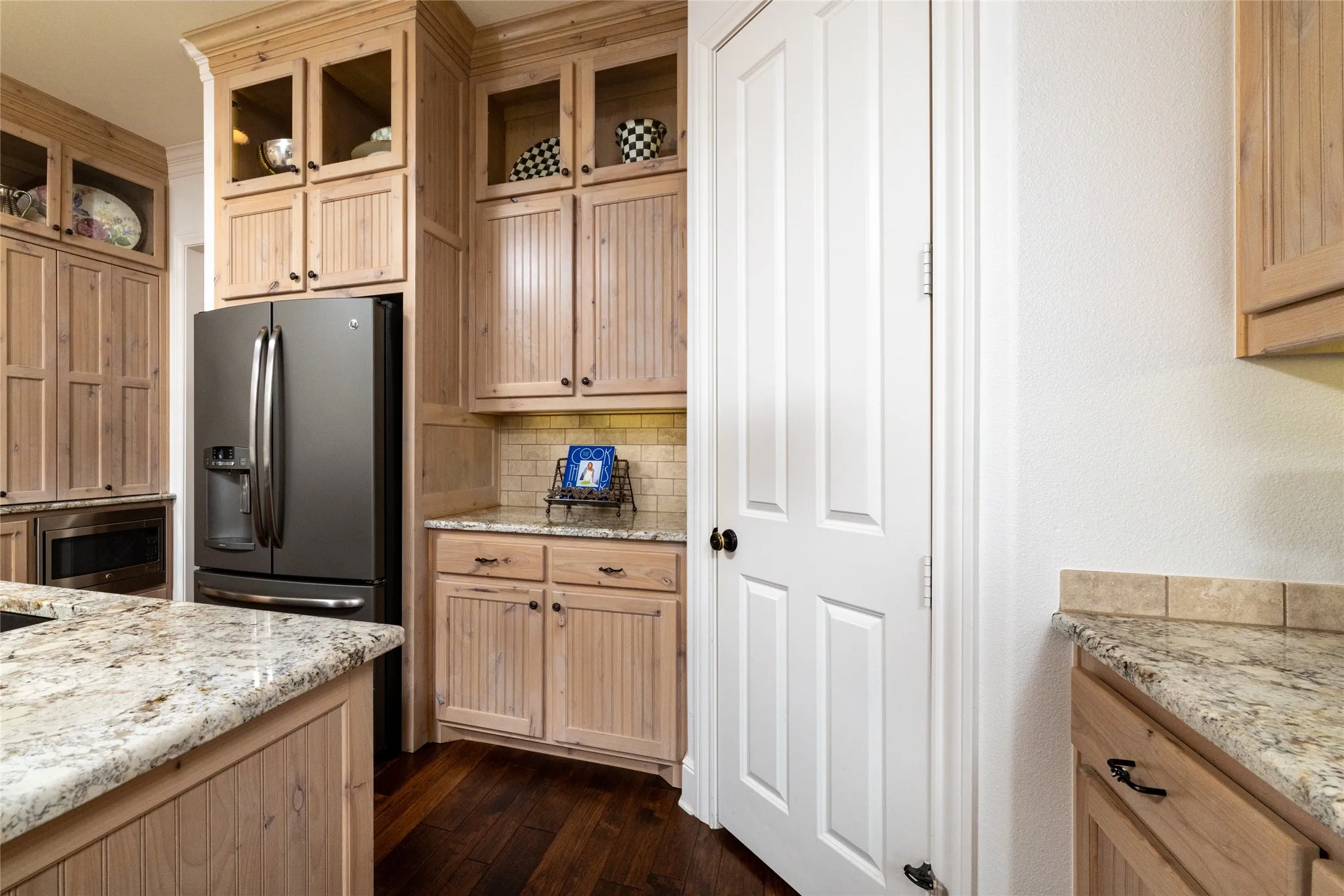 Stainless steel refrigerator, integrated microwave, wood-finish cabinetry, granite countertops, and wood-finish flooring