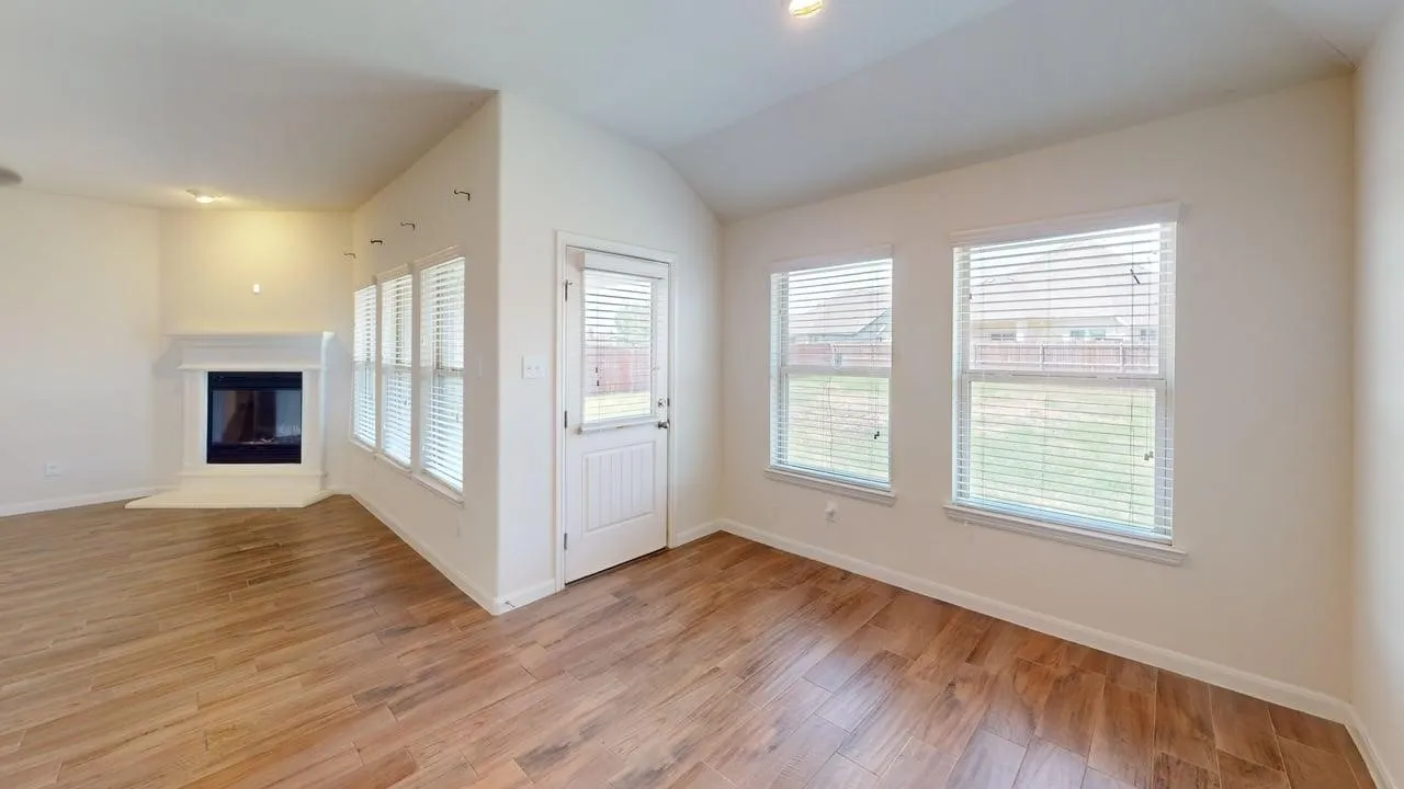 Wood-finish flooring, white walls, multiple windows, a white door, and a built-in fireplace