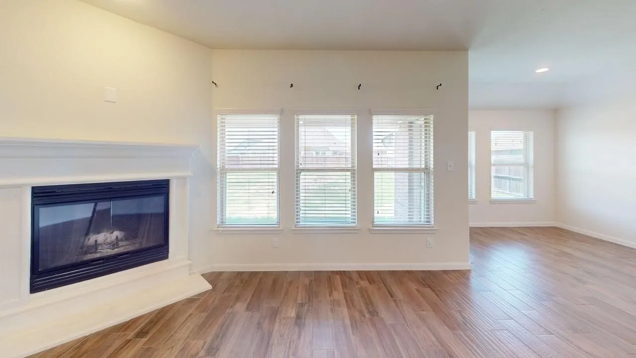 Wood-finish flooring throughout, multiple windows with blinds, a built-in fireplace with a white mantel, recessed lighting, and neutral wall tones