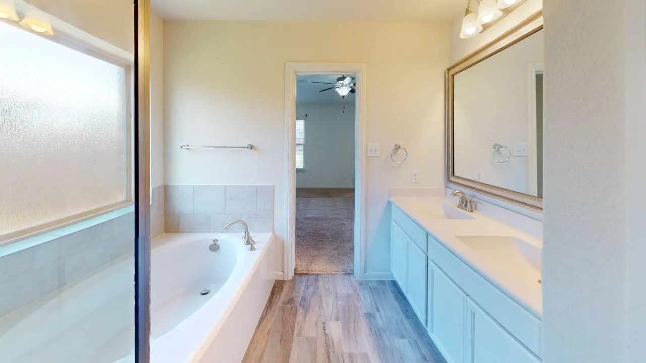 Dual vanity with integrated sinks, framed mirror, wood-finish flooring, and a built-in tub with tile surround