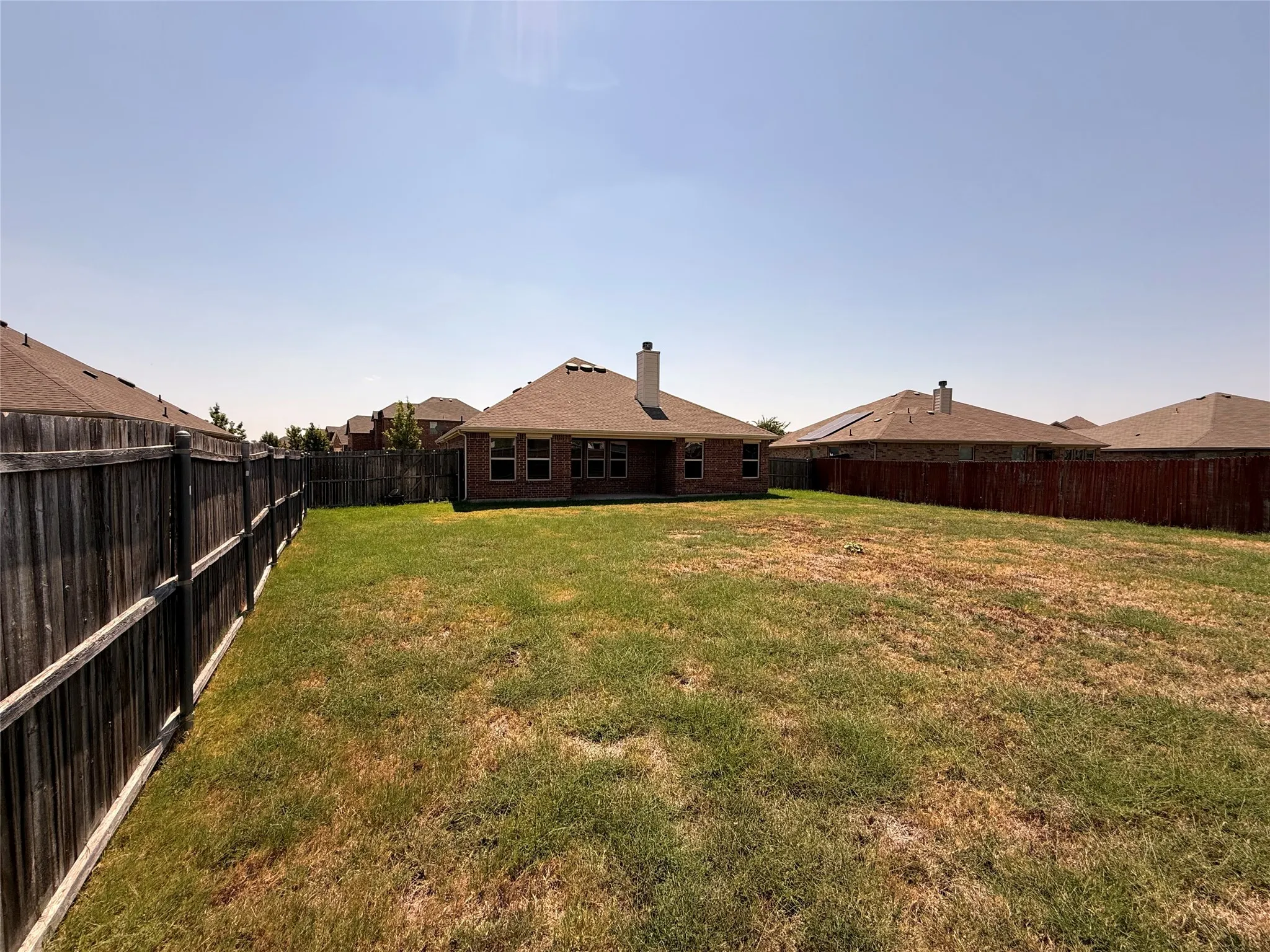 Expansive backyard with a wood privacy fence, a brick exterior on the dwelling, multiple windows, and a chimney