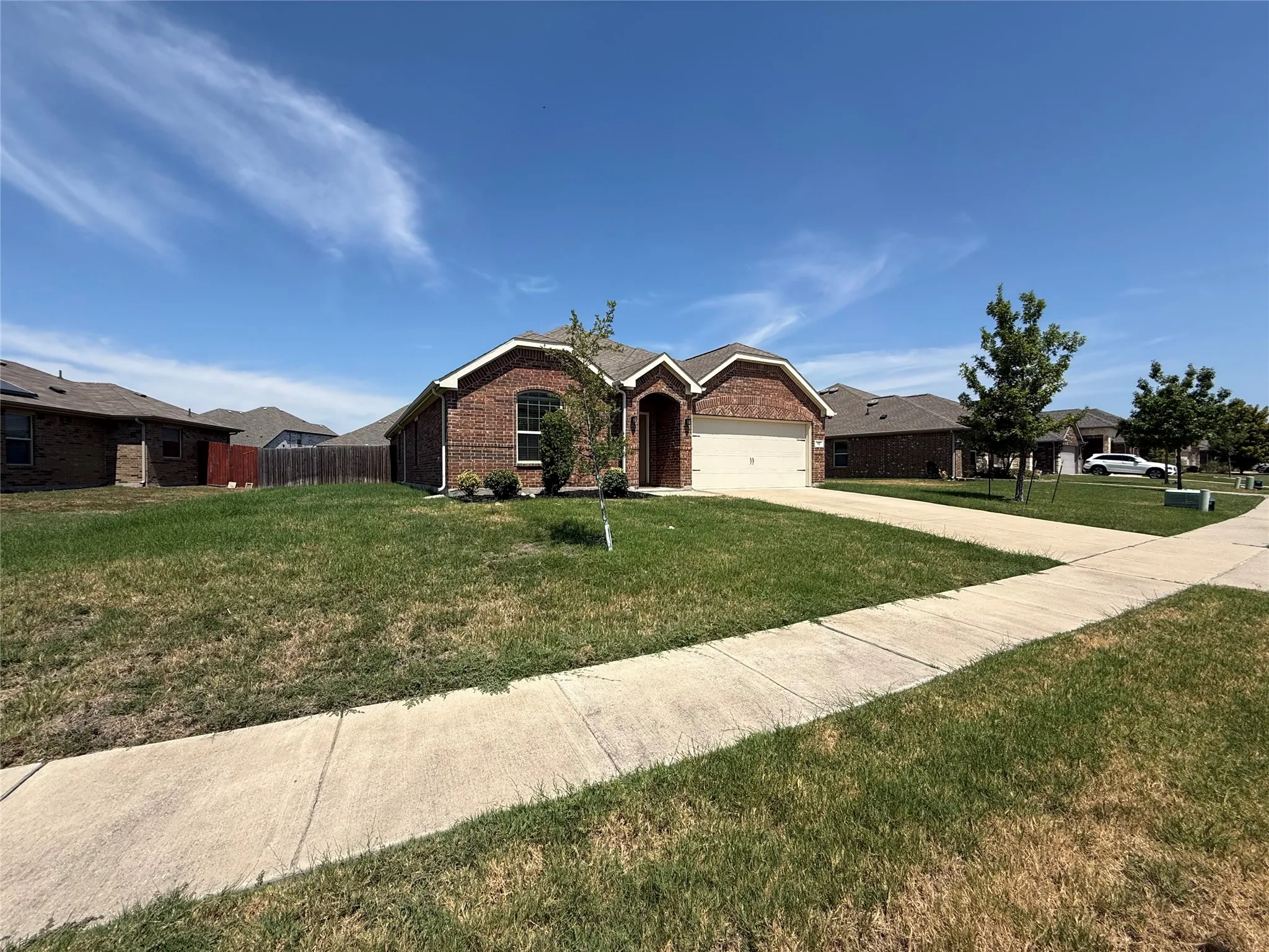 Brick exterior with an arched entry, attached garage, concrete driveway, and mature landscaping