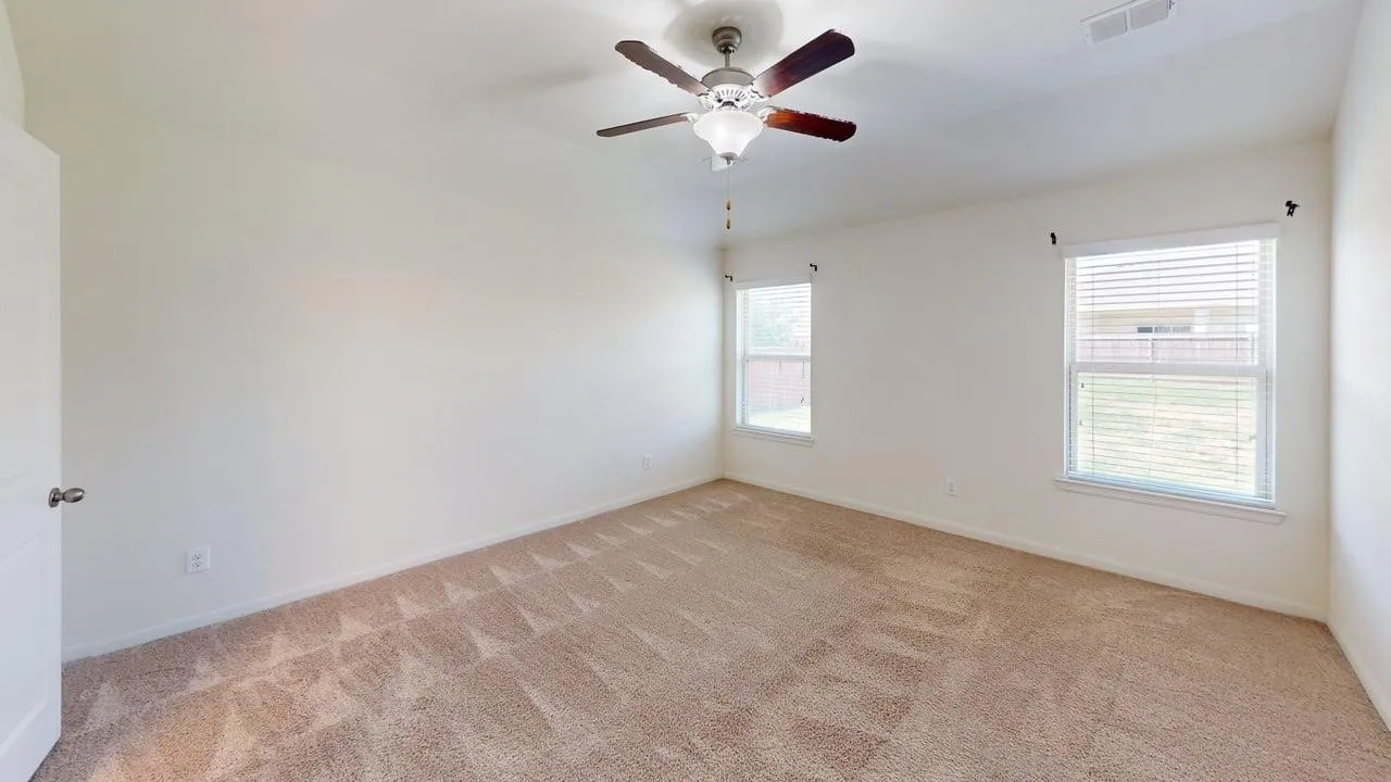 Neutral tone wall color, ceiling fan with light fixture, two windows with blinds, and carpeted flooring