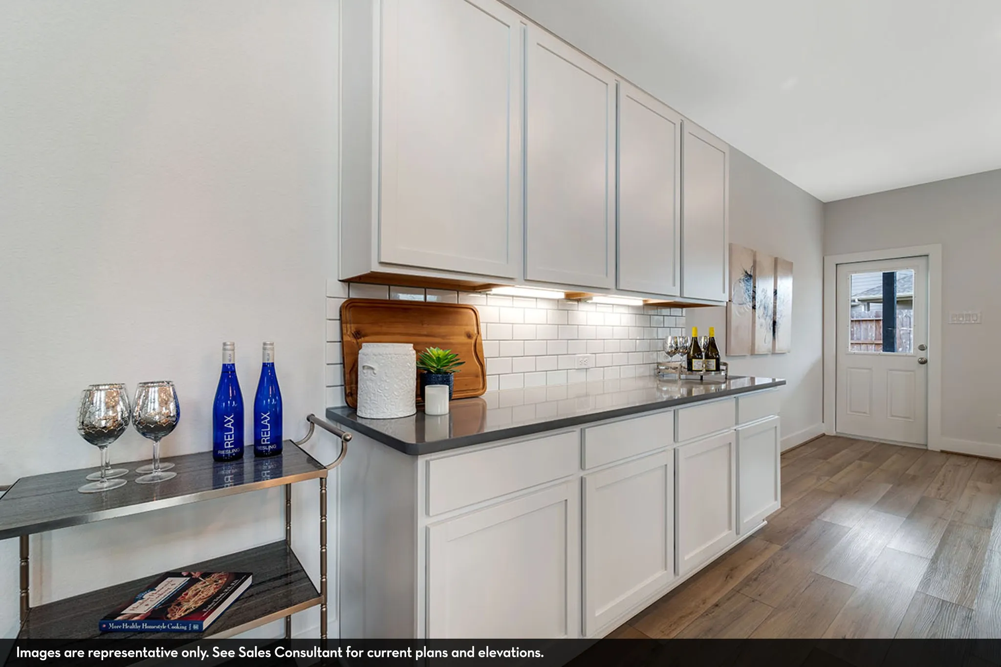 White shaker cabinetry, subway tile backsplash, dark-toned countertop, under-cabinet lighting, and wood-finish flooring