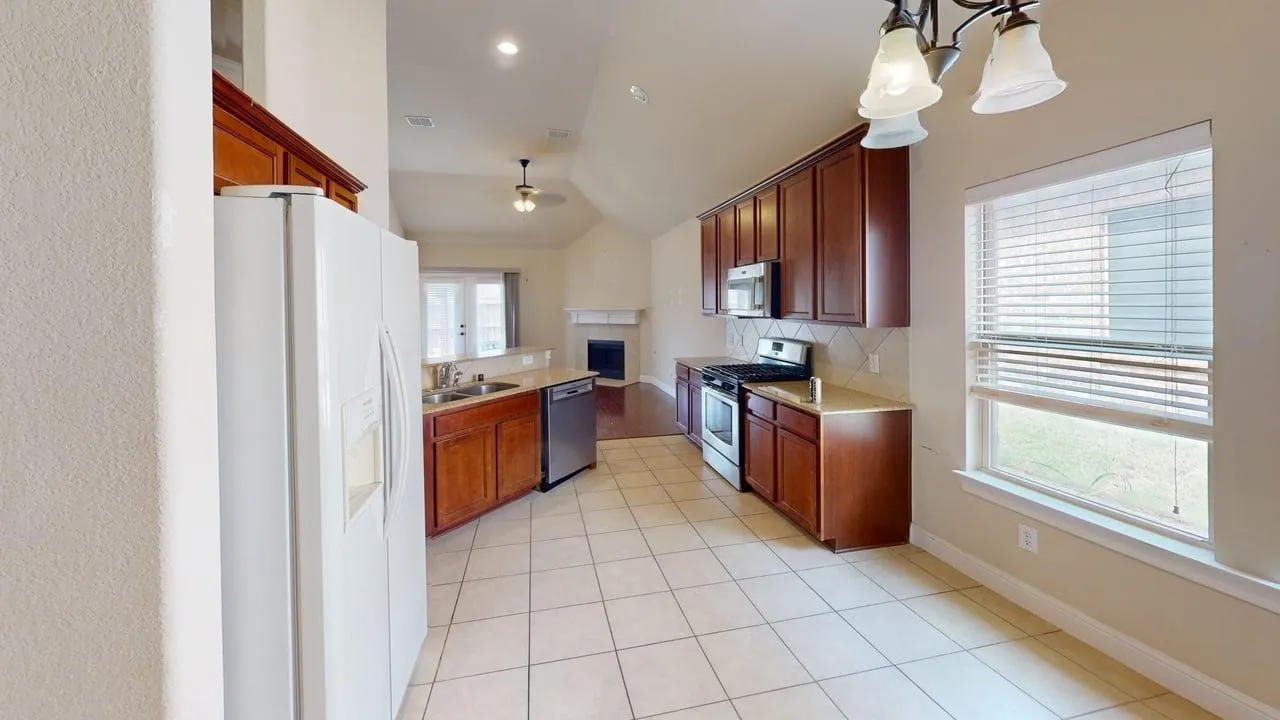 Open-concept kitchen with tile flooring, wood-finish cabinetry, stainless steel appliances, and a dining area with a window