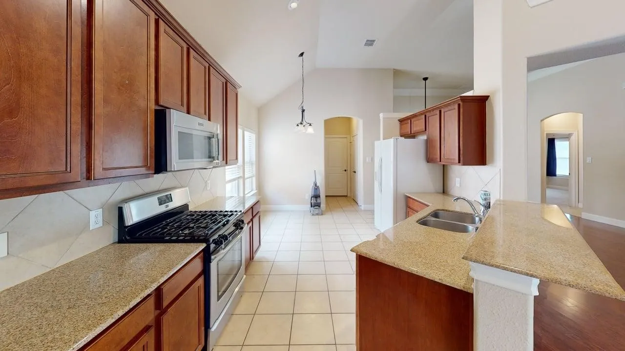 Kitchen featuring wood cabinetry, stainless steel appliances, speckled countertops, a double basin sink, and tile flooring
